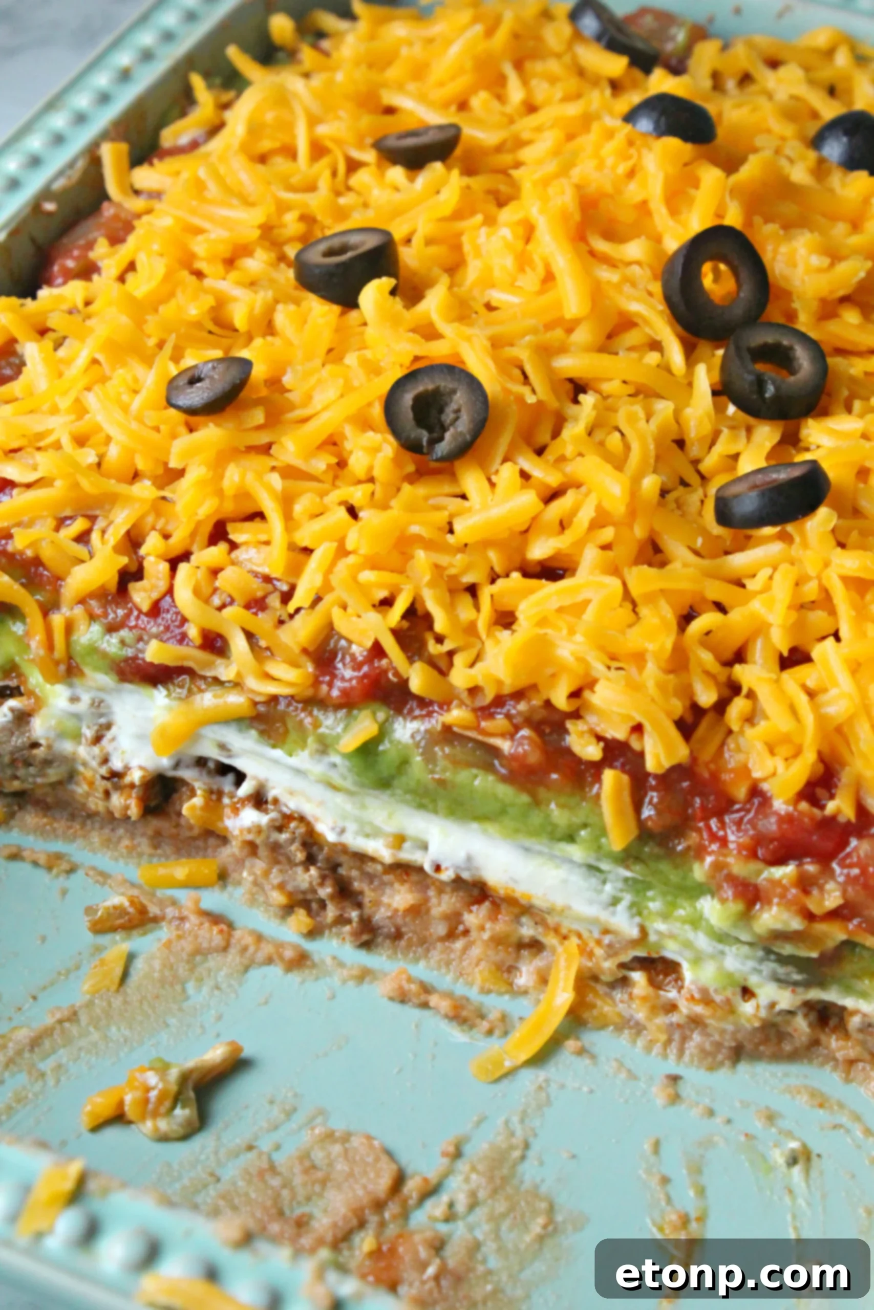 7 layer taco dip with half missing in a blue baking dish