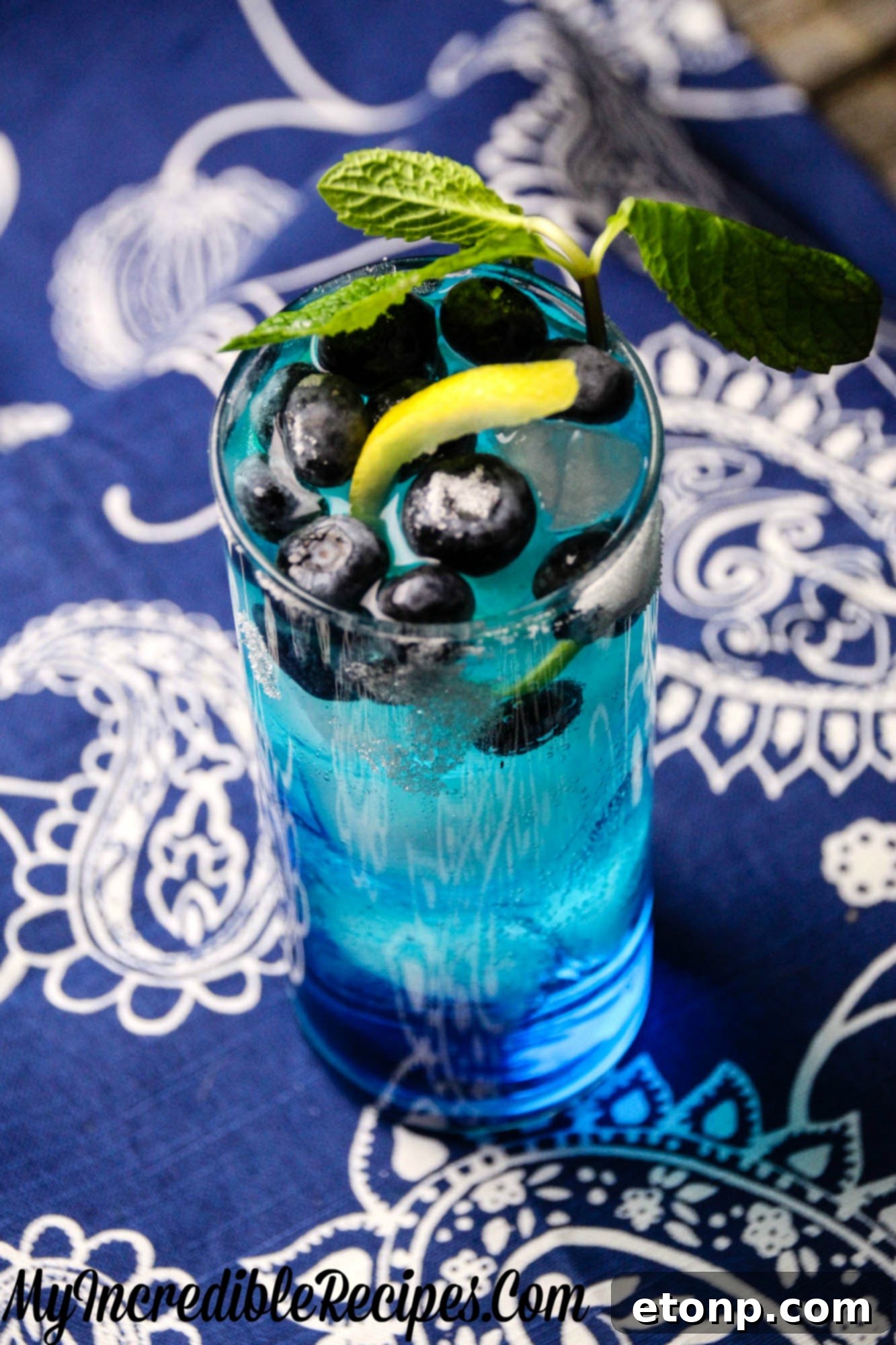 Zingy Blueberry Lemonade 4 Three elegant glasses filled with the vivid blue Bangin' Blueberry Lemonade, garnished with lemon slices and mint sprigs