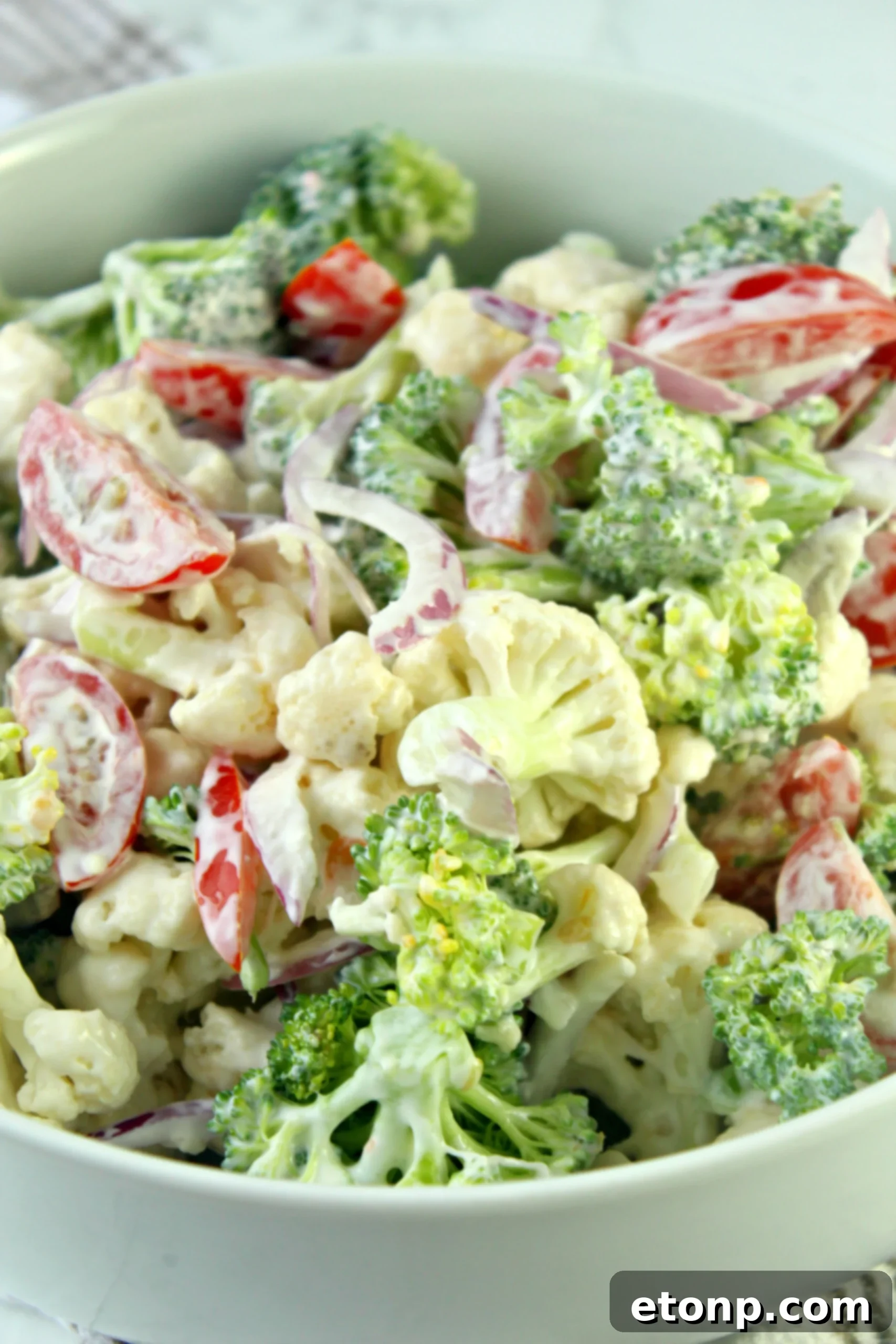 Hands preparing vegetables for Christmas Salad, showing chopped broccoli and cauliflower on a cutting board, emphasizing quick prep.