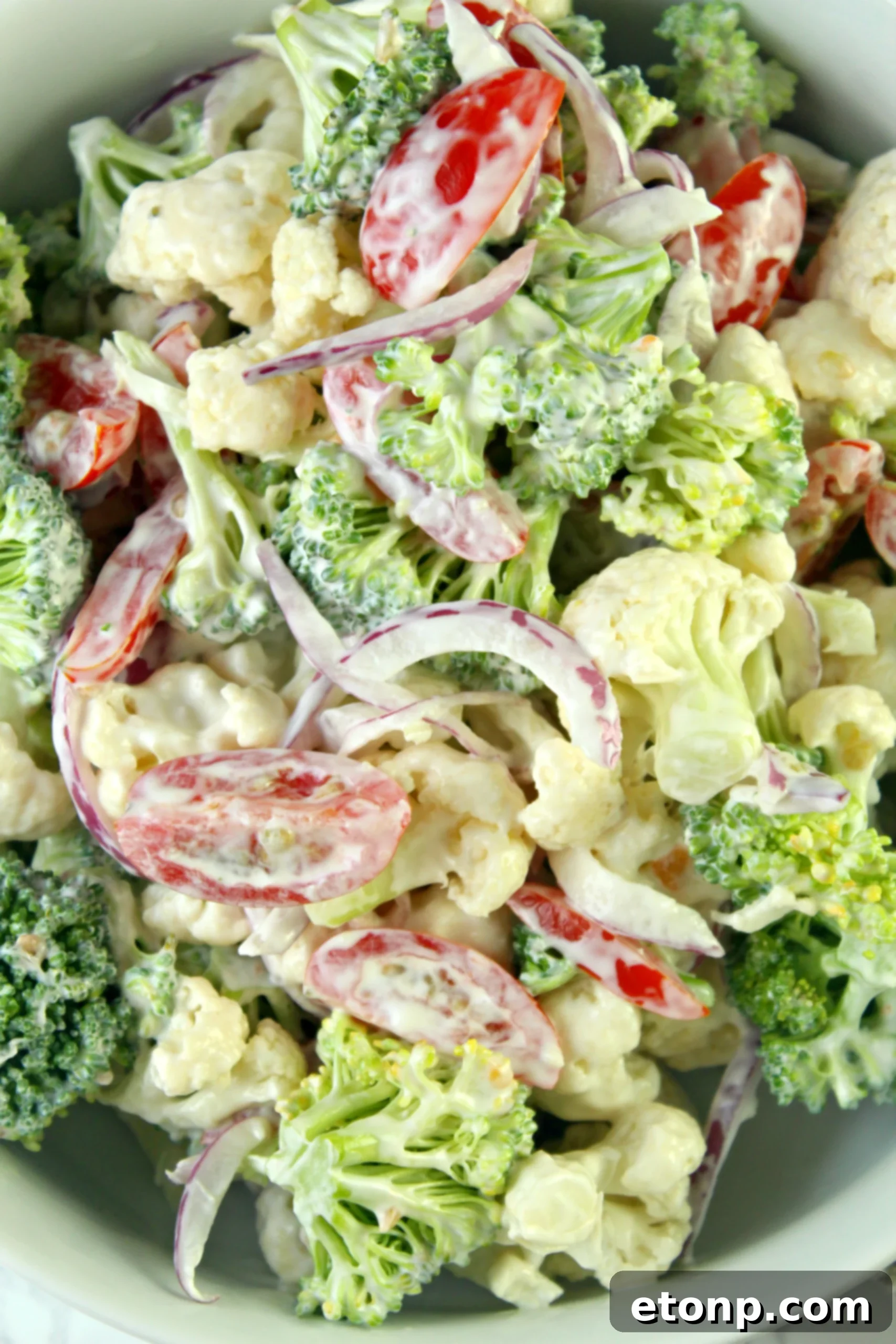 A close-up of Christmas Salad ingredients, showing fresh broccoli, cauliflower, cherry tomatoes, and red onion in a bowl, before mixing.