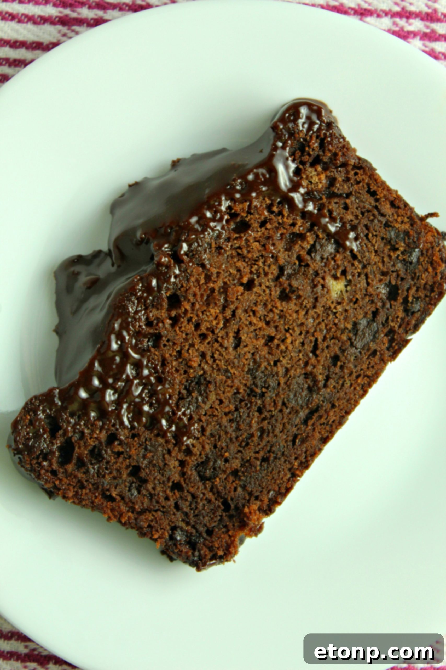 A close-up of a hand drizzling melted chocolate glaze over a loaf of double chocolate banana bread.