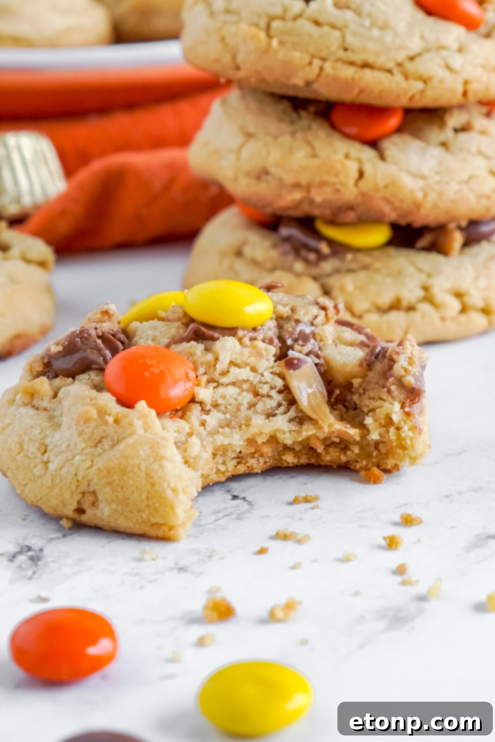 A close-up of two hands reaching for a Reese's Peanut Butter Cup Cookie on a cooling rack.