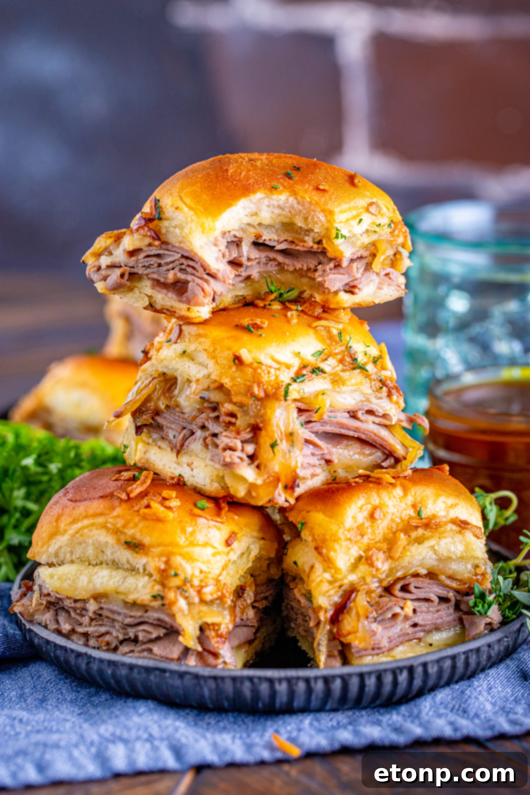 French Dip Sliders piled high with a bite taken out of one, served on a black plate.