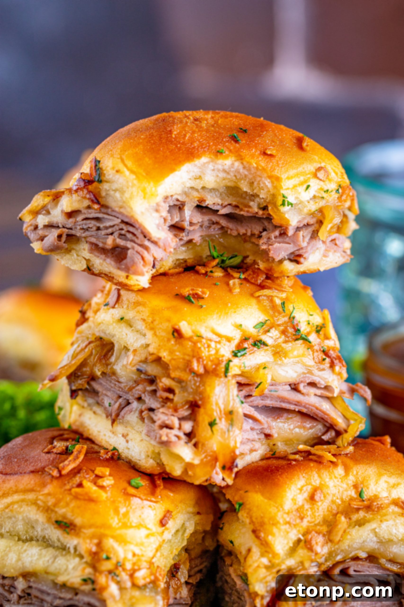 French Dip Sliders piled high on a black plate, with one slider having a bite taken.