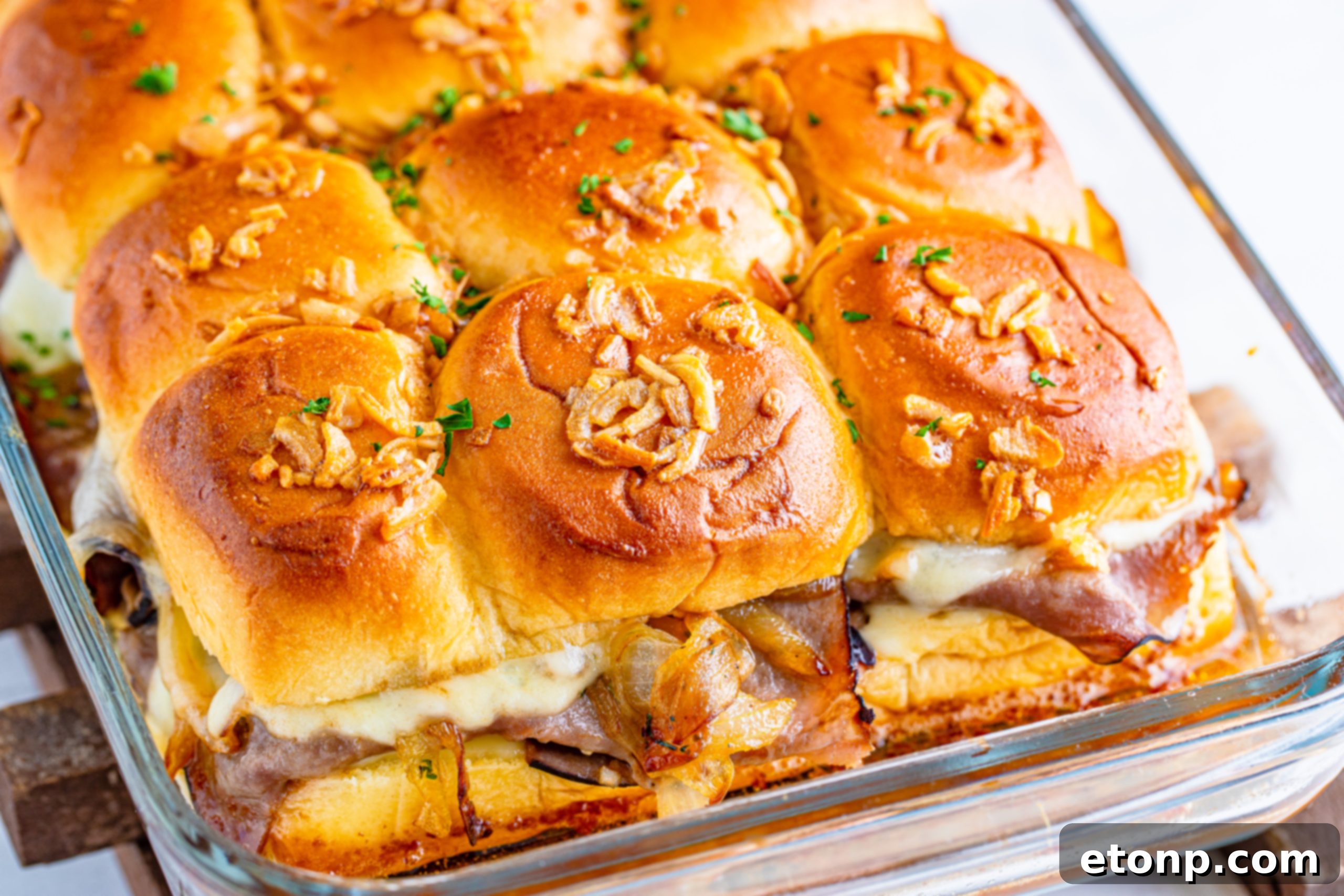 French Dip Sliders uncut in the baking dish with caramelized onions spread on top, ready for baking.