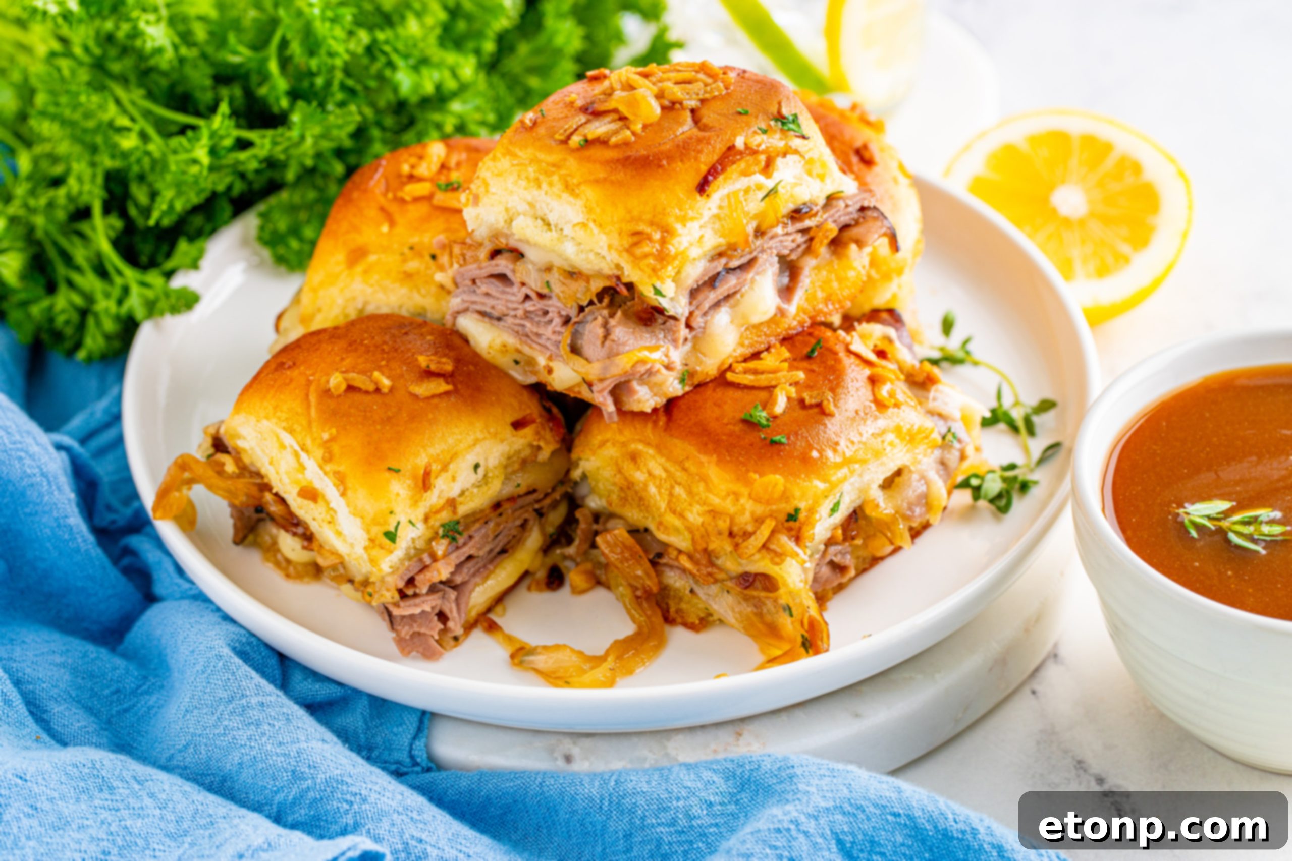 French Dip Sliders piled on a white plate, showcasing the cheesy, beefy layers.