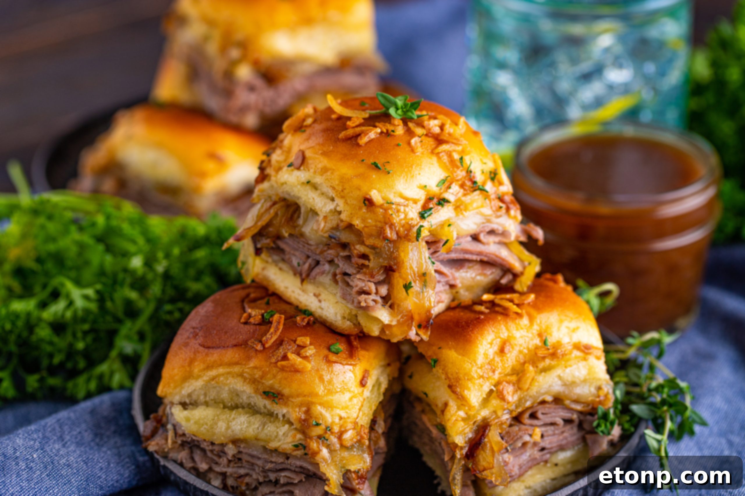 Three French Dip Sliders arranged on a black plate with a small container of au jus next to them.