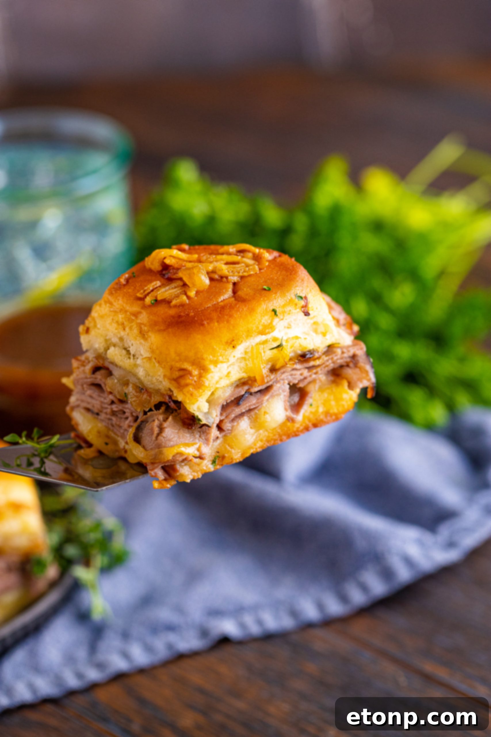 A single French Dip Slider being lifted off a baking dish with a spatula.