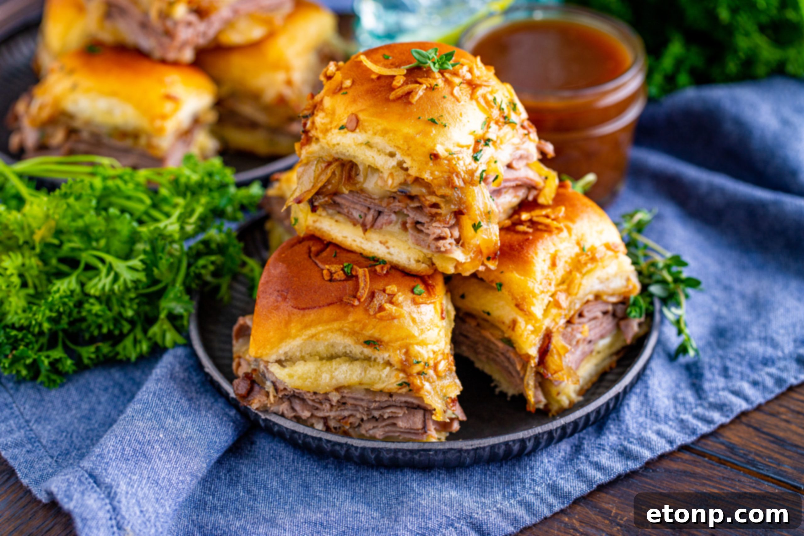 French Dip Sliders piled on a black plate, set on a dark wood table with a blue napkin.