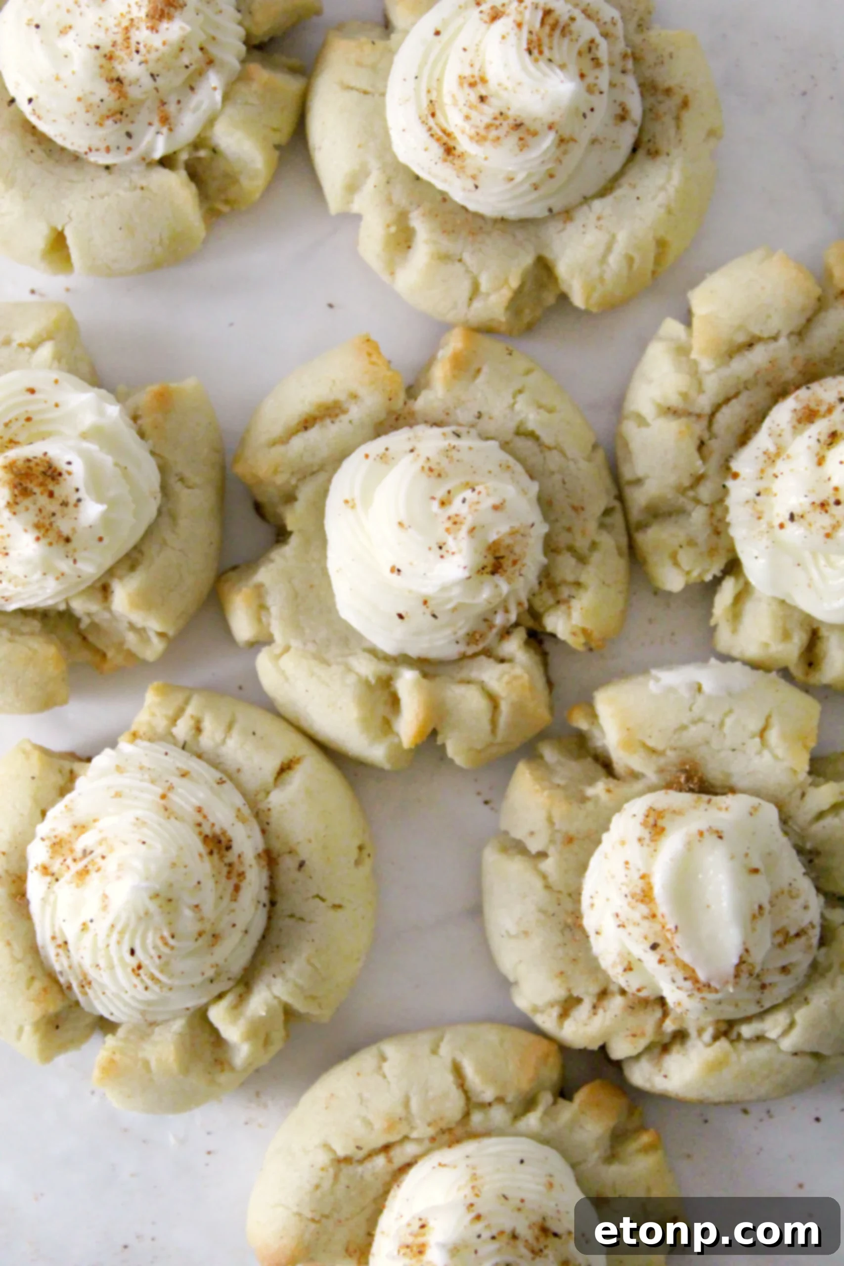 Close-up of freshly frosted Eggnog Thumbprint Cookies with Rum Buttercream, dusted with nutmeg, beautifully arranged on a white serving plate, embodying holiday cheer.