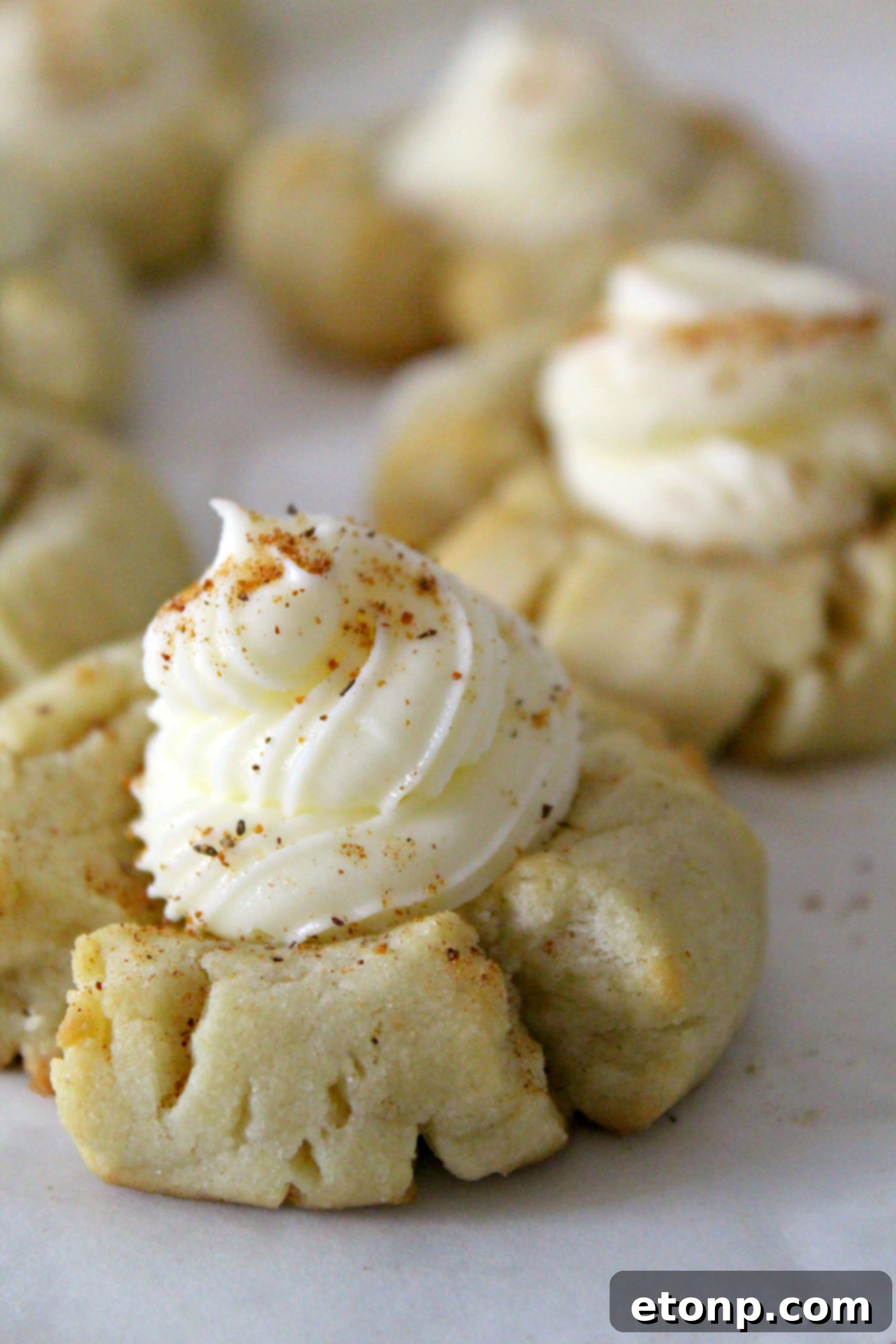 A perfectly frosted Eggnog Thumbprint Cookie with a generous dollop of rum buttercream and a sprinkle of nutmeg, ready to be enjoyed.