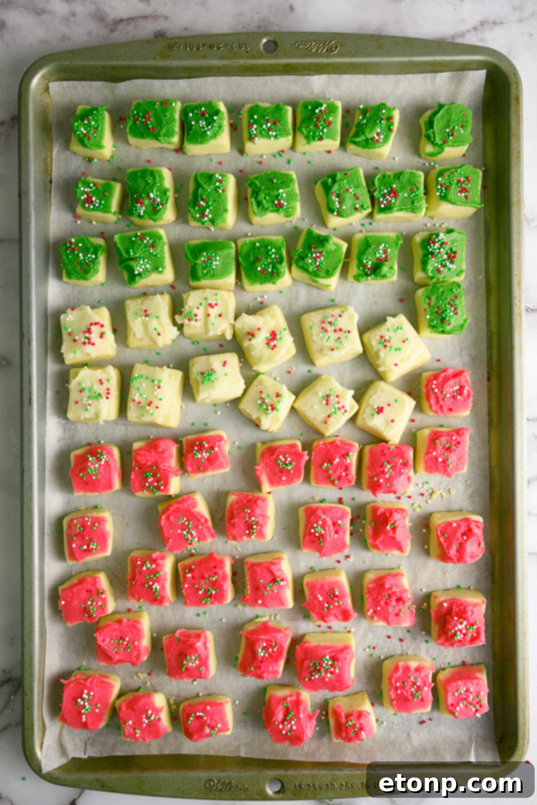A festive spread of various Christmas Sugar Cookie Bites with different frosting colors and sprinkles on a wooden tray, ready for serving.