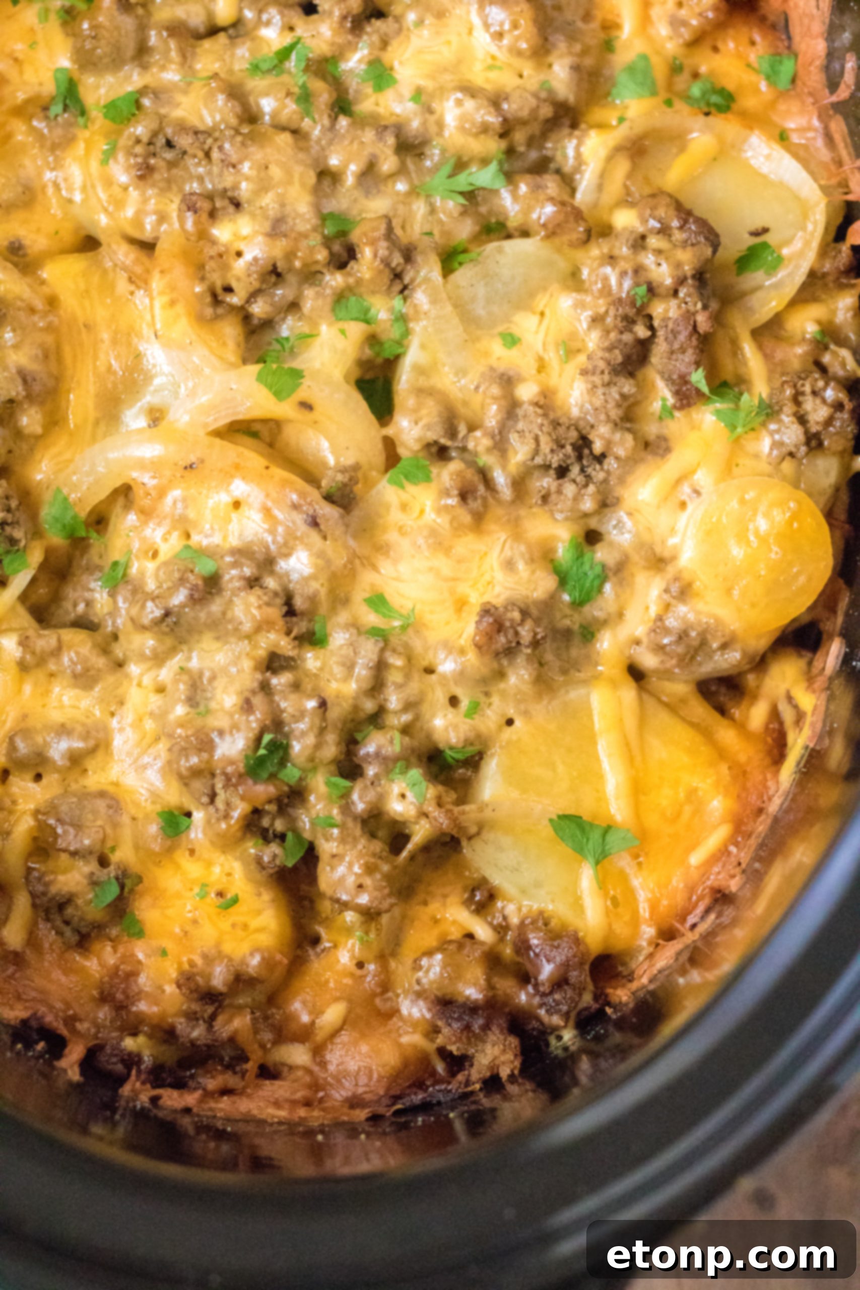 A serving of Slow Cooker Beef and Potato Au Gratin on a plate, showing the layers of beef, potatoes, and melted cheese, garnished with fresh parsley.