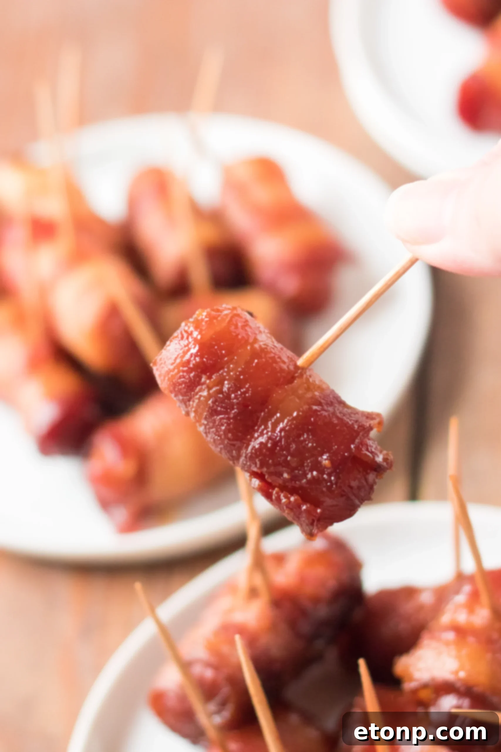 Crock-Pot Candy Bacon Smokies 8 A single Bacon Wrapped Smokie, picked up with a toothpick, showing the caramelized texture.