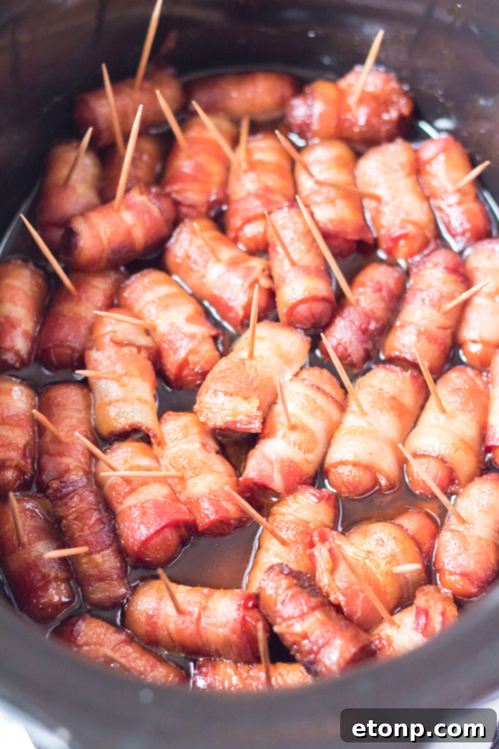 Crock-Pot Candy Bacon Smokies 10 Overhead view of a slow cooker filled with bacon-wrapped smokies, simmering to perfection.