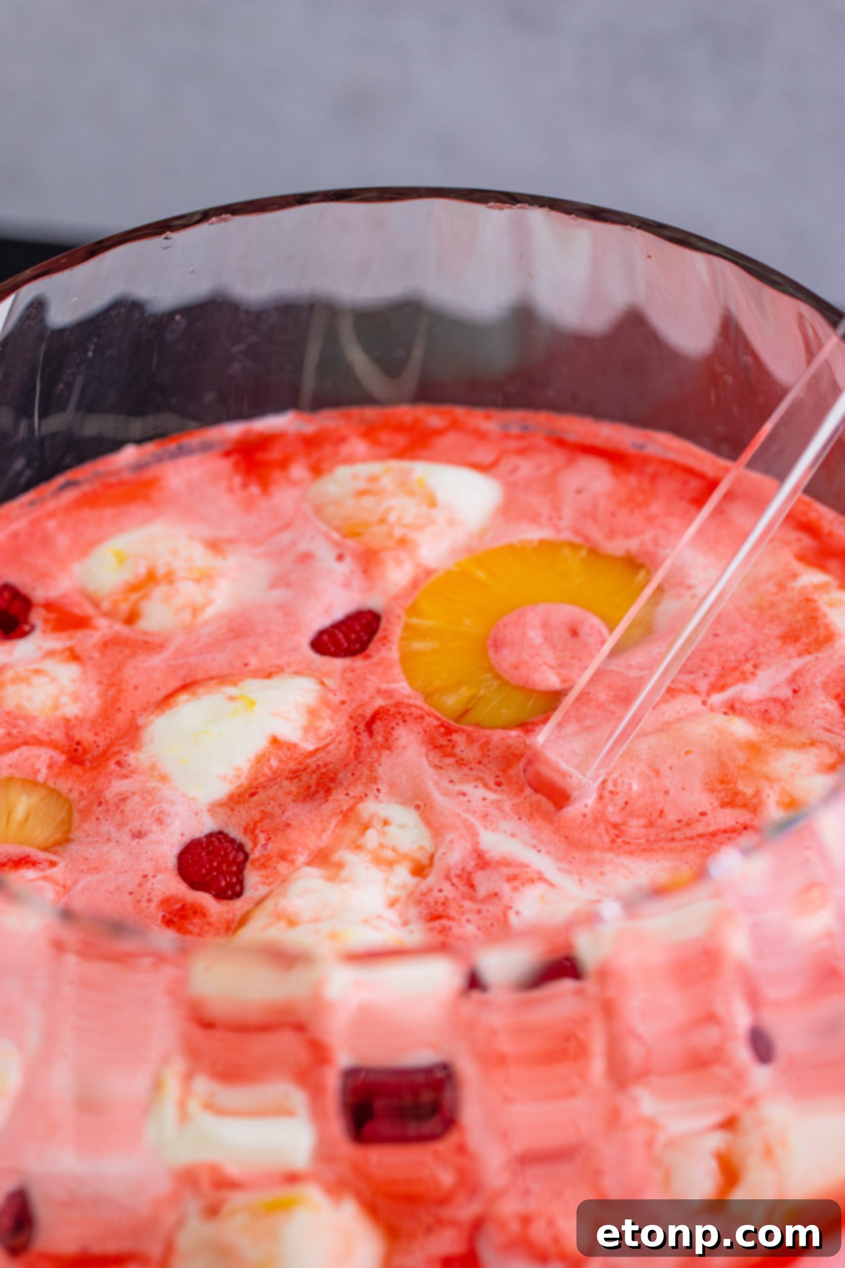 Beautifully presented Boozy Sherbet Punch in a punch bowl with pineapple and raspberry garnishes