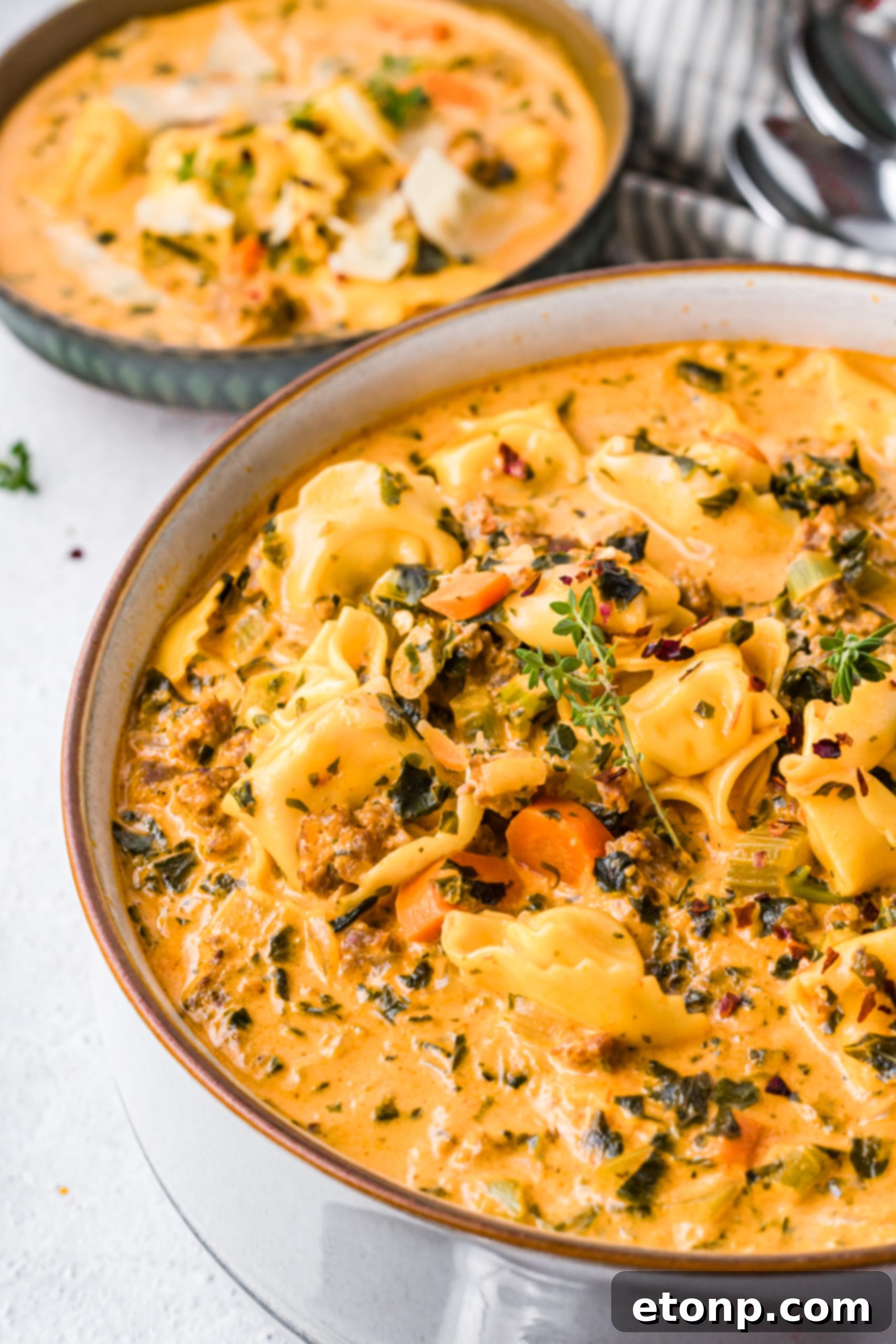 A bowl of creamy tortellini soup garnished with herbs, on a wooden surface.
