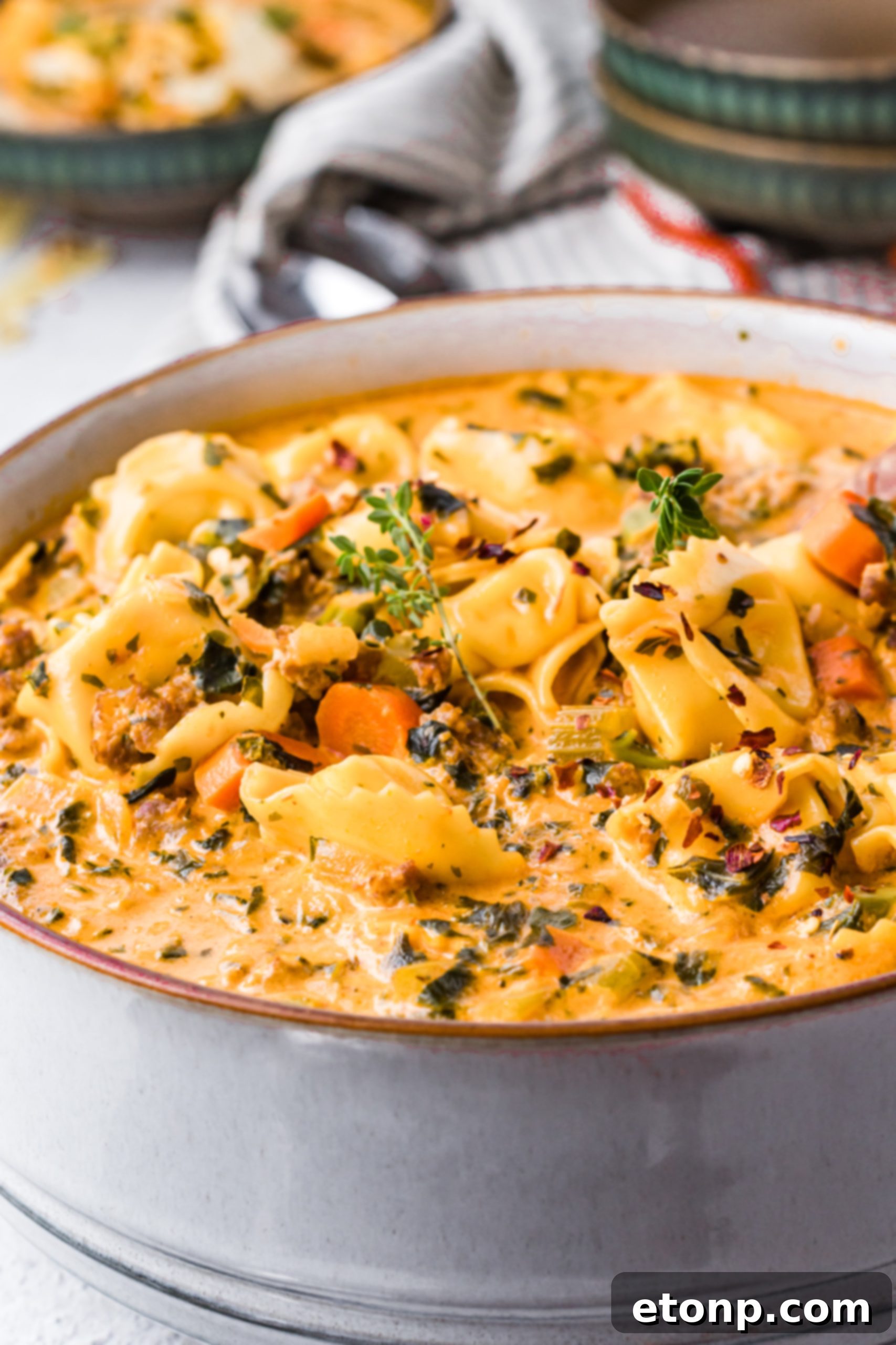 A large serving of creamy tortellini soup in a bowl with a spoon, showing a hearty portion.