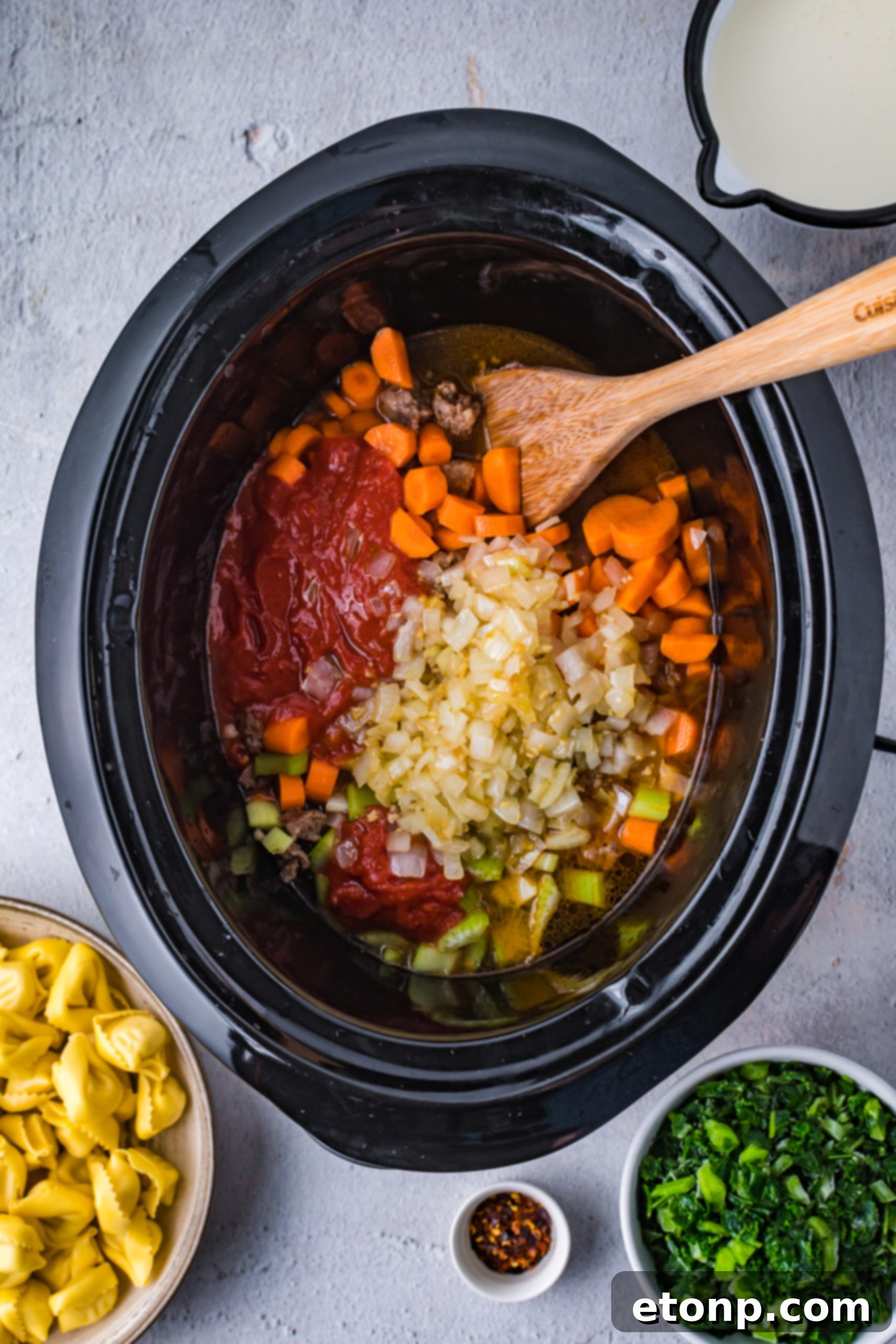 A top-down view of a vibrant slow cooker creamy tortellini soup in a large serving pot.