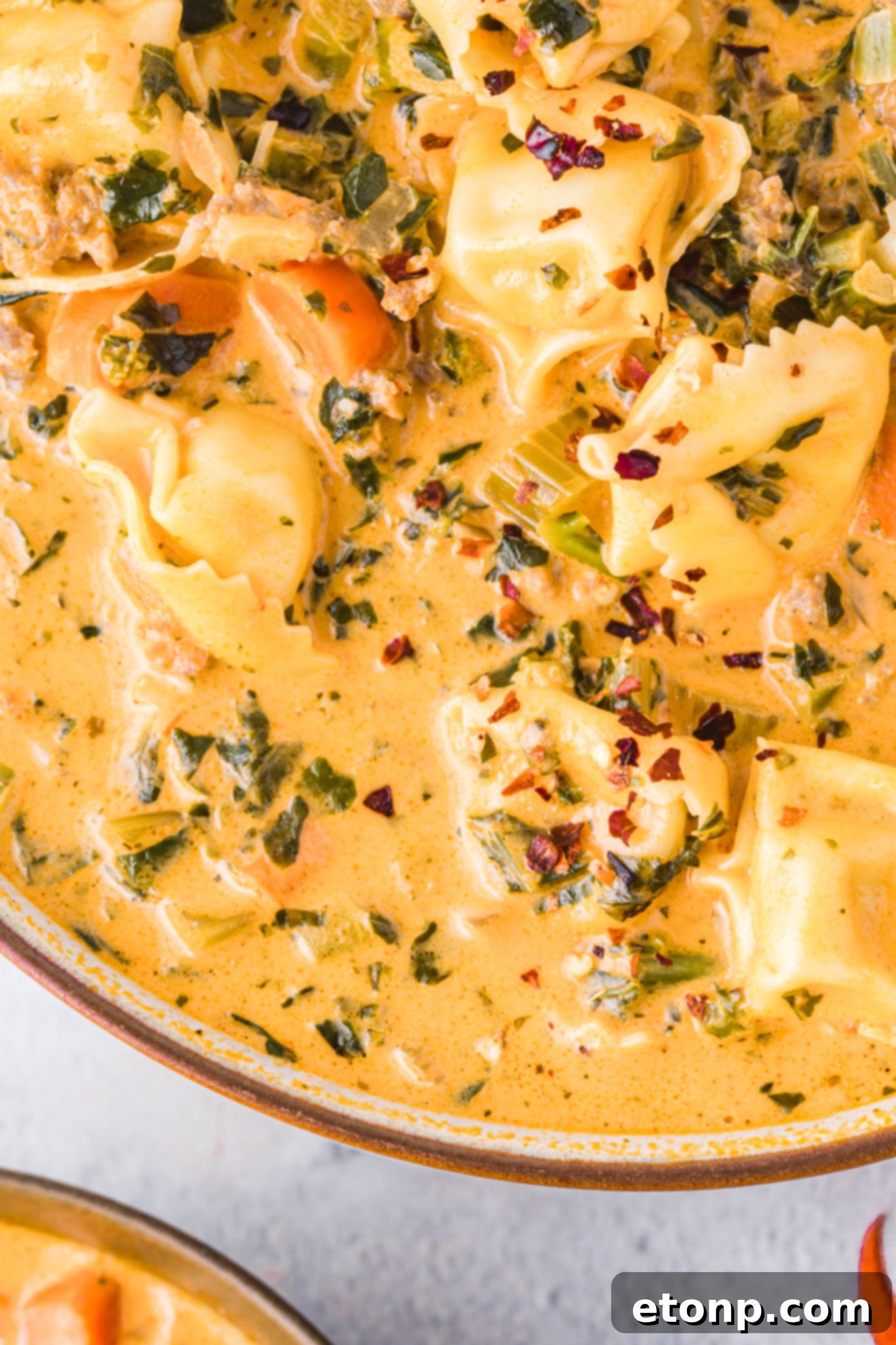 An overhead shot of slow cooker creamy tortellini soup in a large pot, with a serving spoon.
