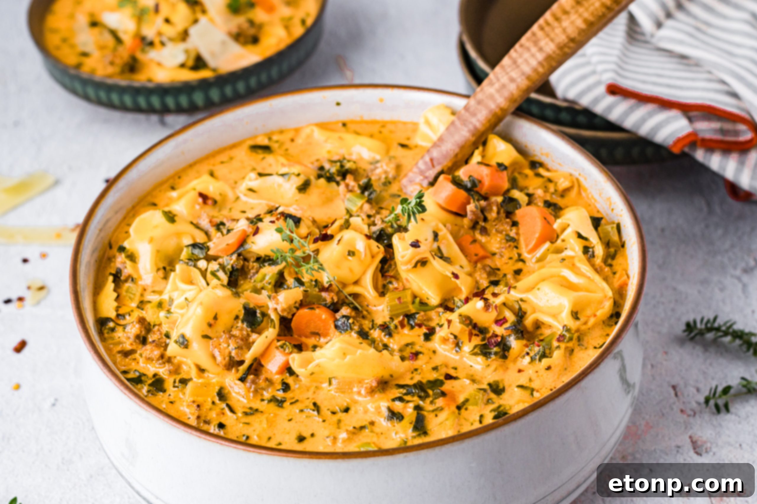 Two bowls of creamy tortellini soup with bread, ready to be served.