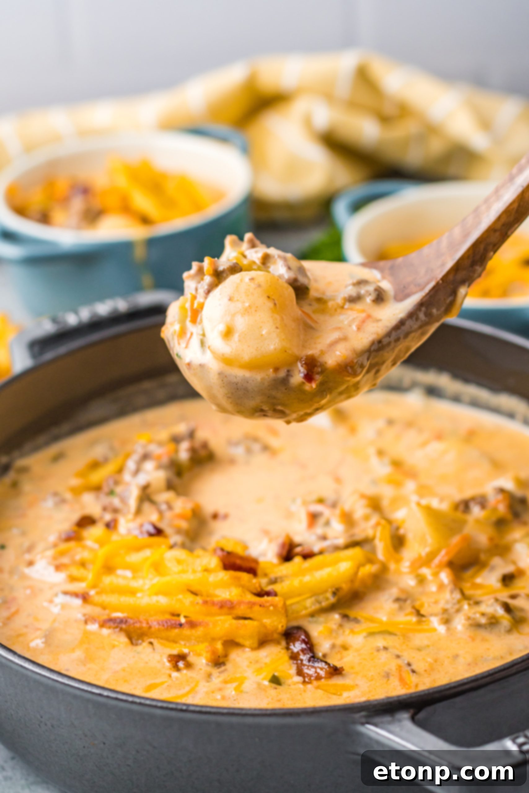 A bowl of slow cooker cheeseburger soup garnished with cheddar cheese, bacon, and green onions, served on a wooden board.