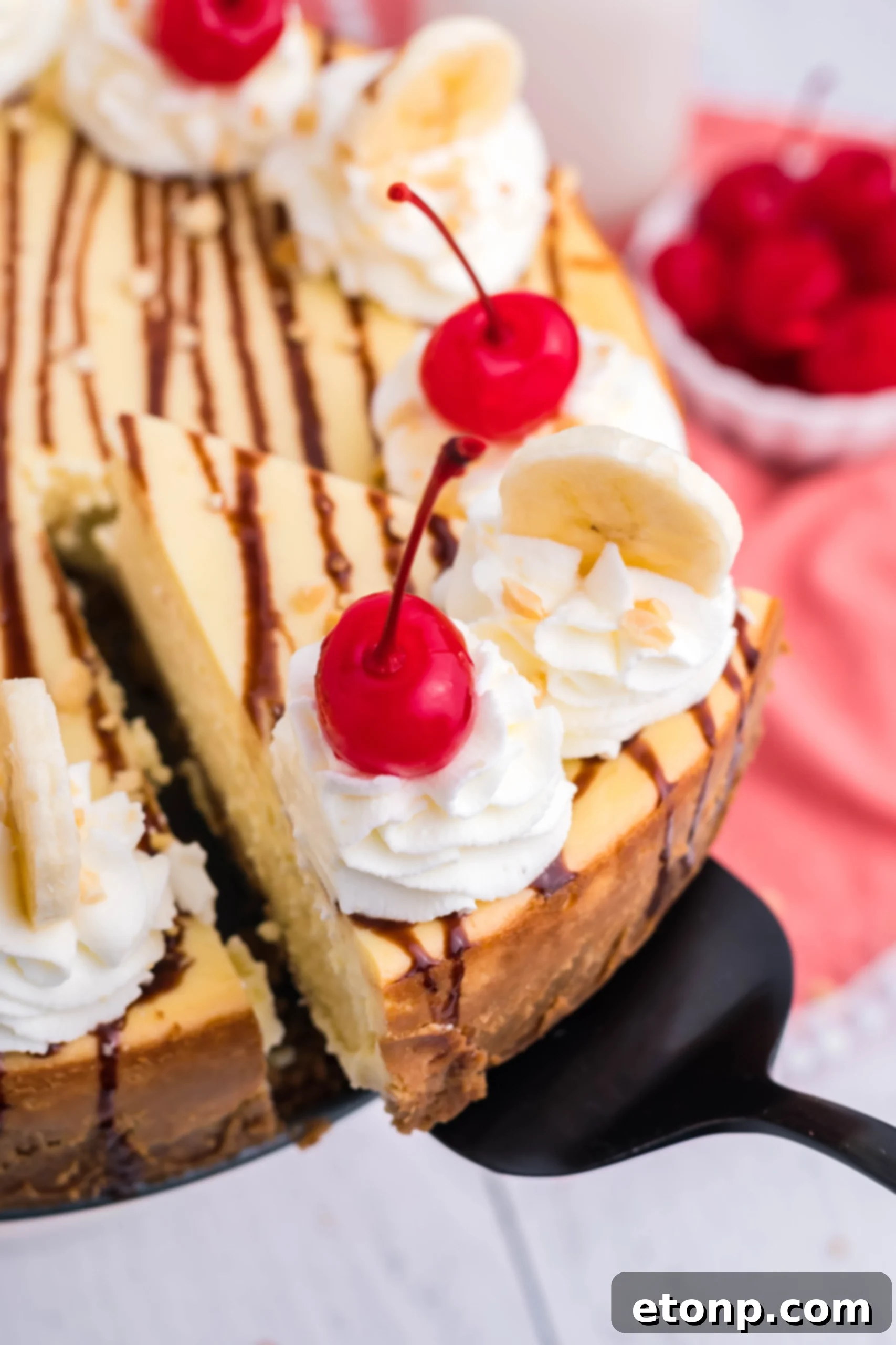 A vibrant slice of Banana Split Cheesecake, showcasing layers of creamy banana filling, graham cracker crust, and colorful toppings like whipped cream, chocolate syrup, banana slices, and a cherry.