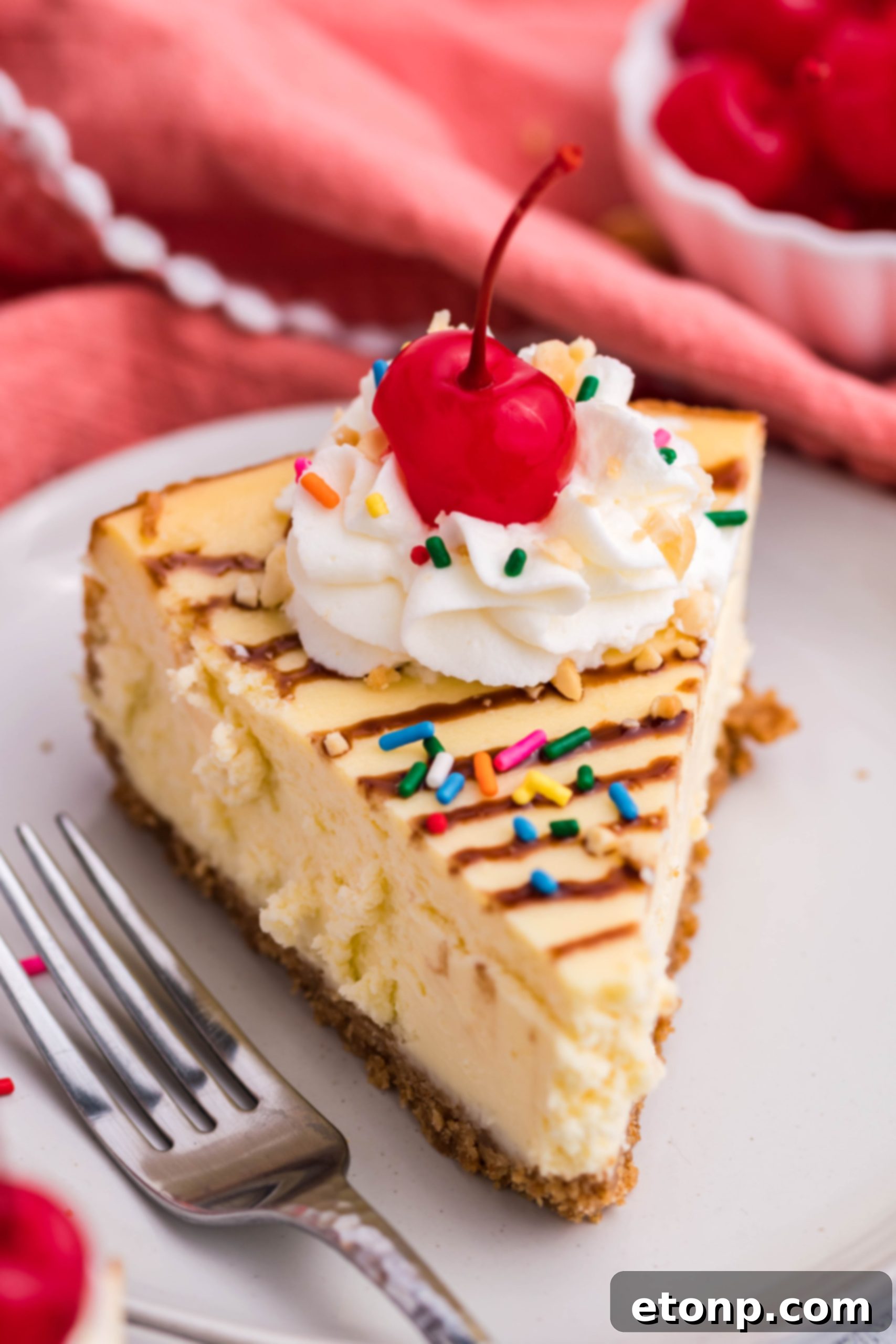 A close-up of a full Banana Split Cheesecake, showcasing its rich texture and artful arrangement of toppings. The golden crust is visible around the edges, framing the creamy filling and its delicious decorations.