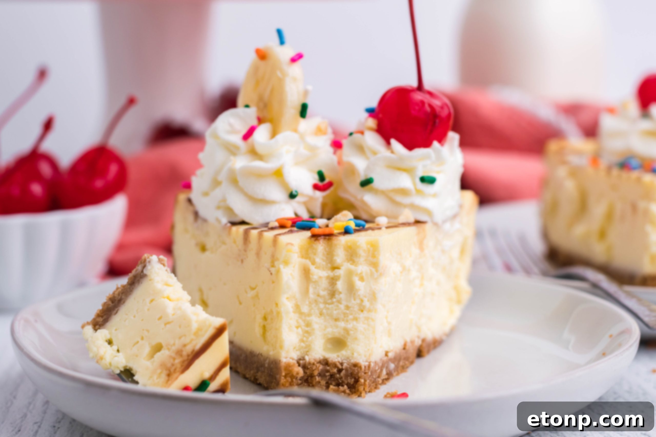 A generously topped slice of Banana Split Cheesecake, with visible layers of crust, creamy filling, and a cascade of chocolate syrup, whipped cream, cherries, and banana slices.