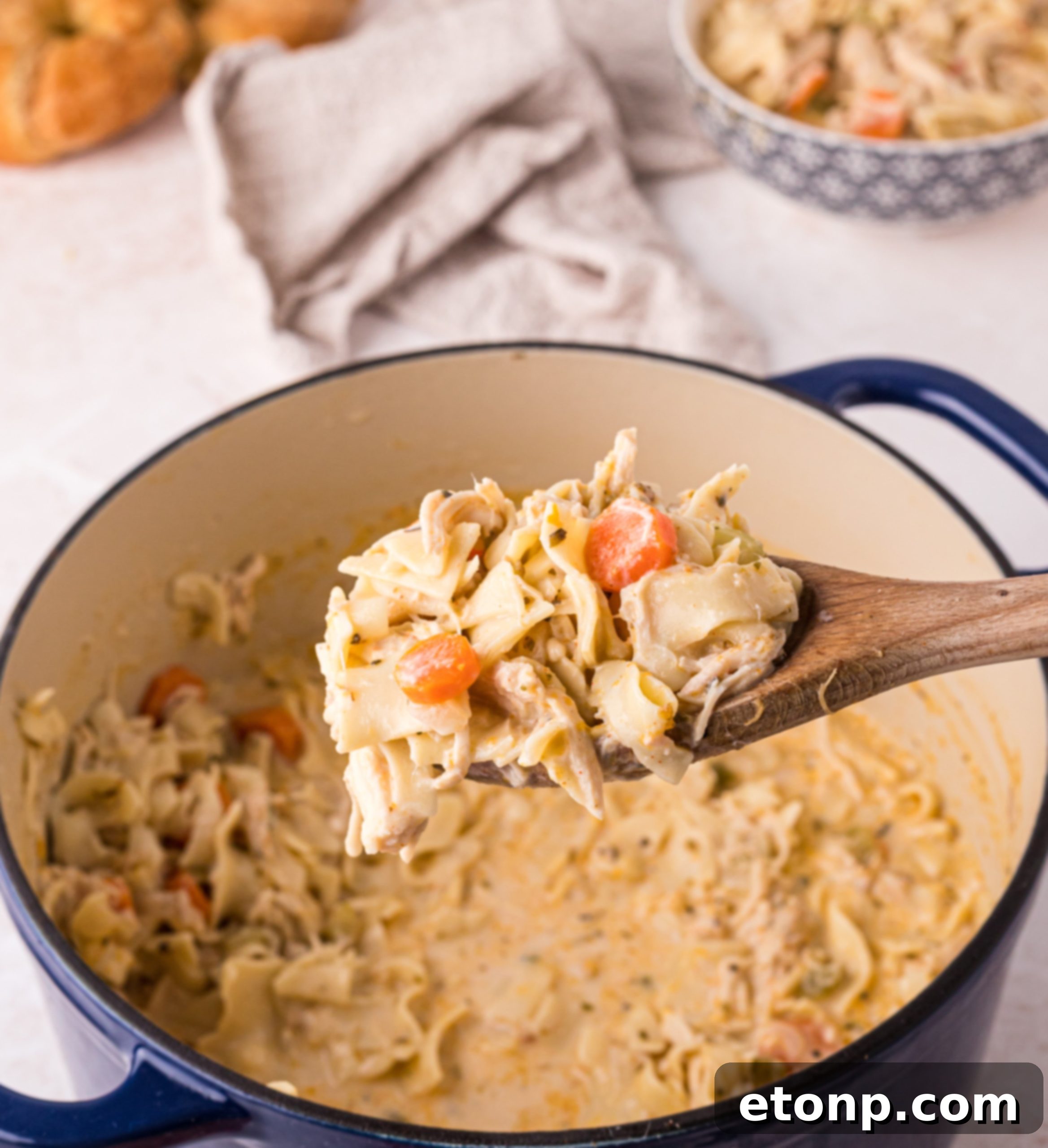 A steaming bowl of creamy chicken noodle soup, garnished with fresh parsley, on a rustic wooden table.
