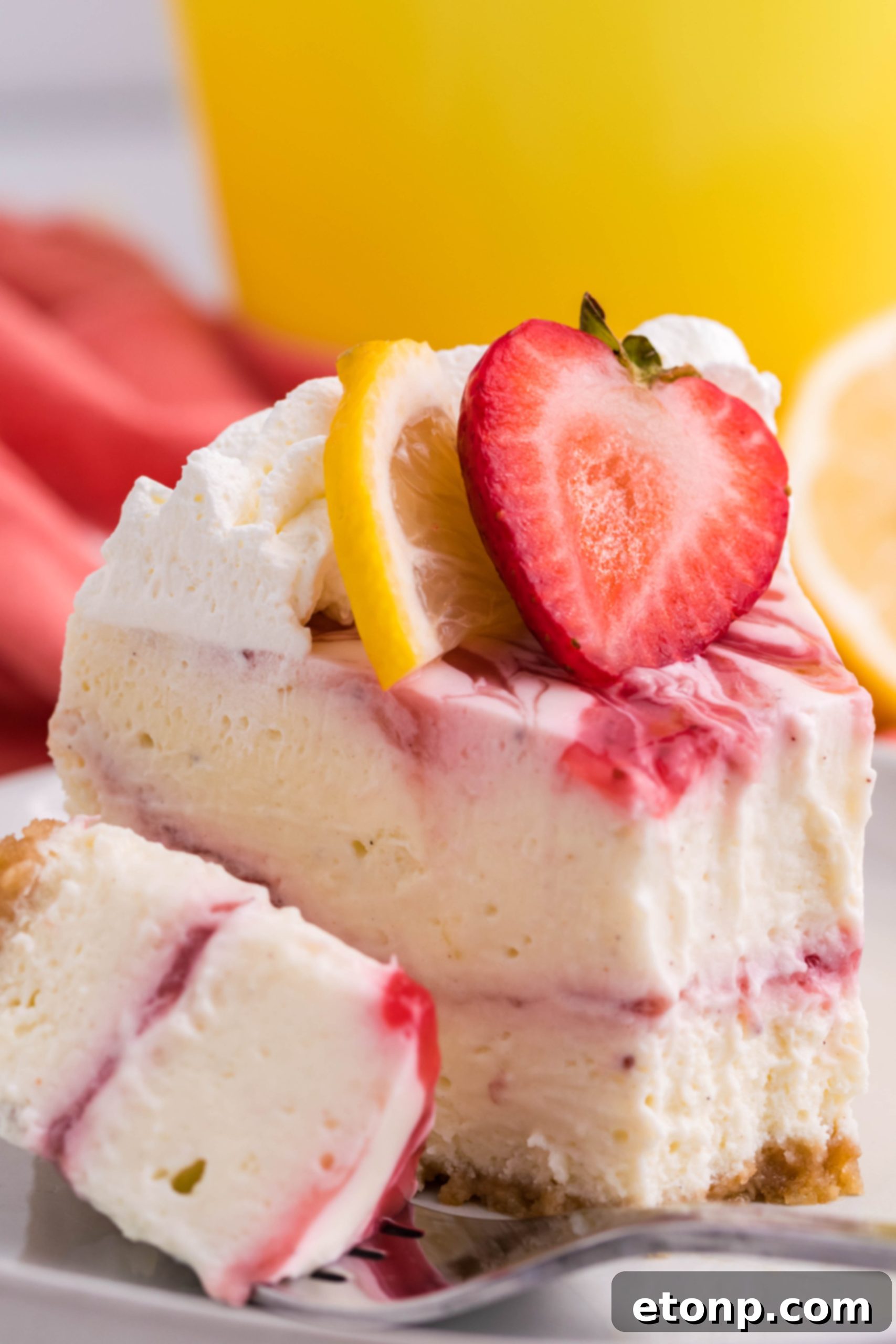 A vibrant slice of Strawberry Lemon RumChata Cheesecake garnished with fresh strawberries and lemon slices, ready to be enjoyed.