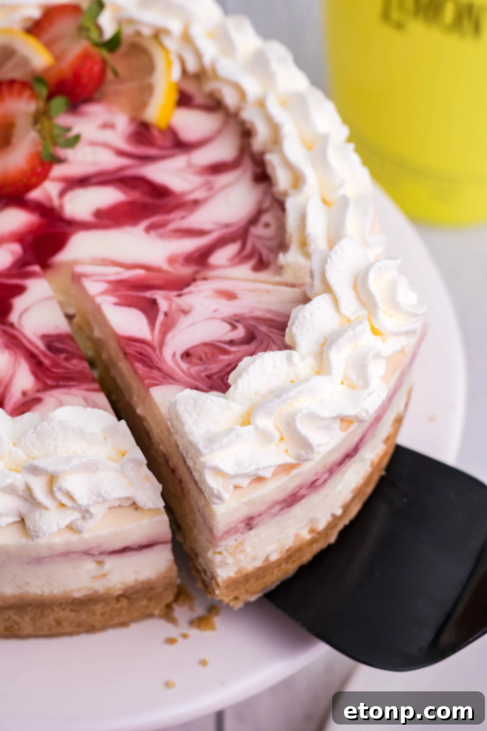 A captivating side view of the Strawberry Lemon RumChata Cheesecake, artfully emphasizing its impressive height, flawlessly smooth sides, and the delicate texture of its Nilla Wafer crust.