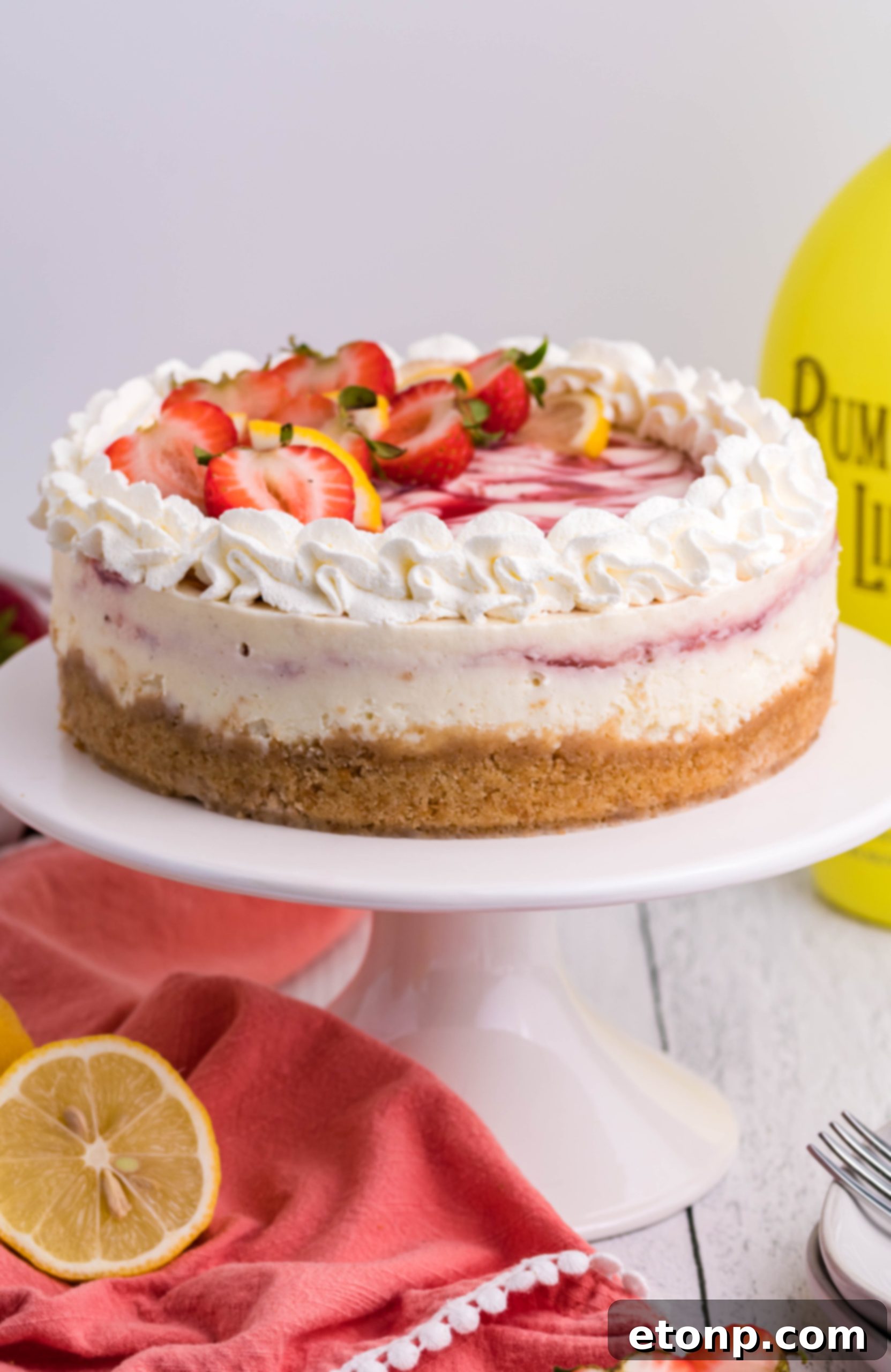 A tantalizing top-down view of a whole Strawberry Lemon RumChata Cheesecake, showcasing its creamy filling and a beautifully intricate strawberry swirl.