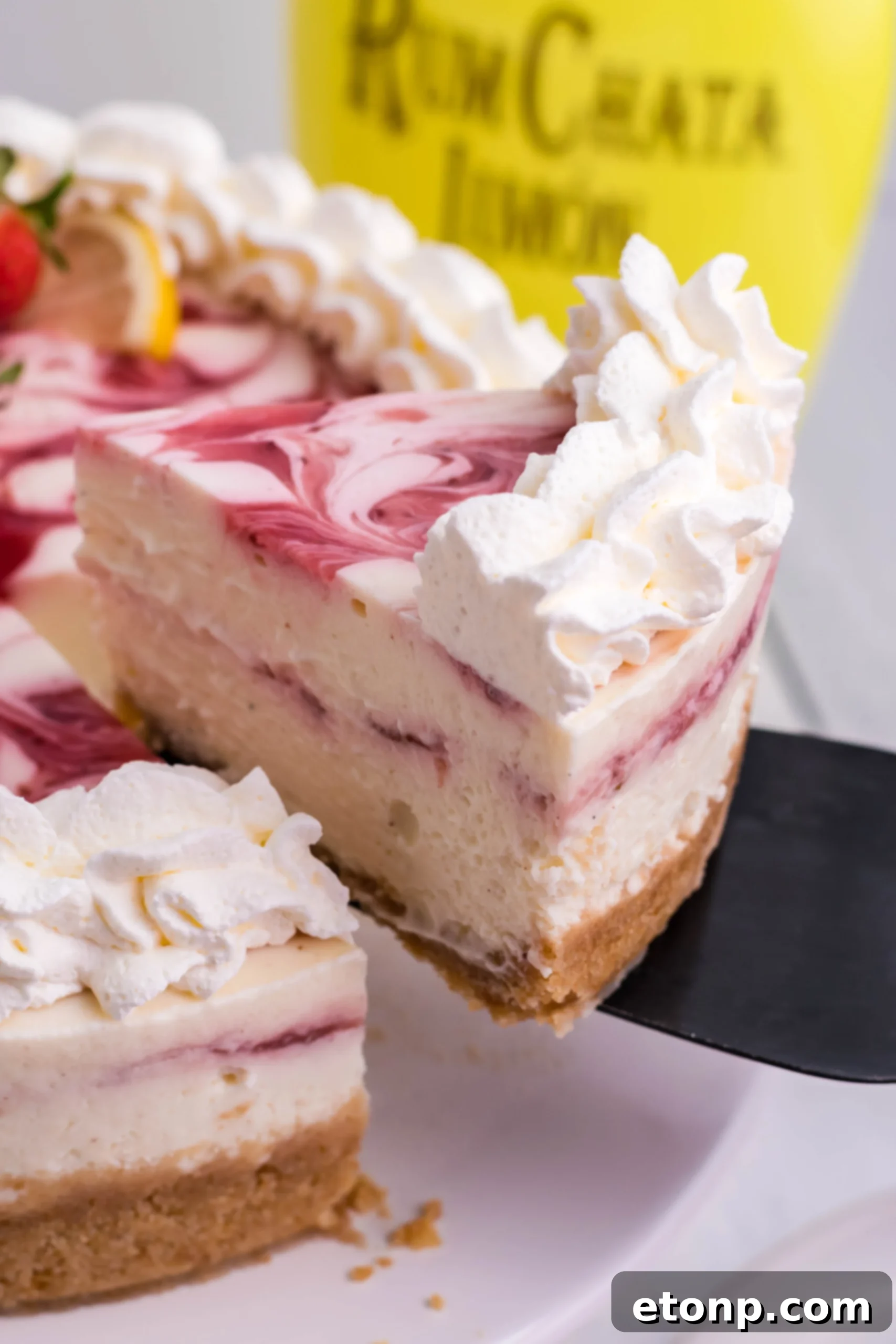 A beautifully presented slice of Strawberry Lemon RumChata Cheesecake, featuring a distinct, vibrant strawberry swirl within the creamy filling, poised on a white plate with a fork.