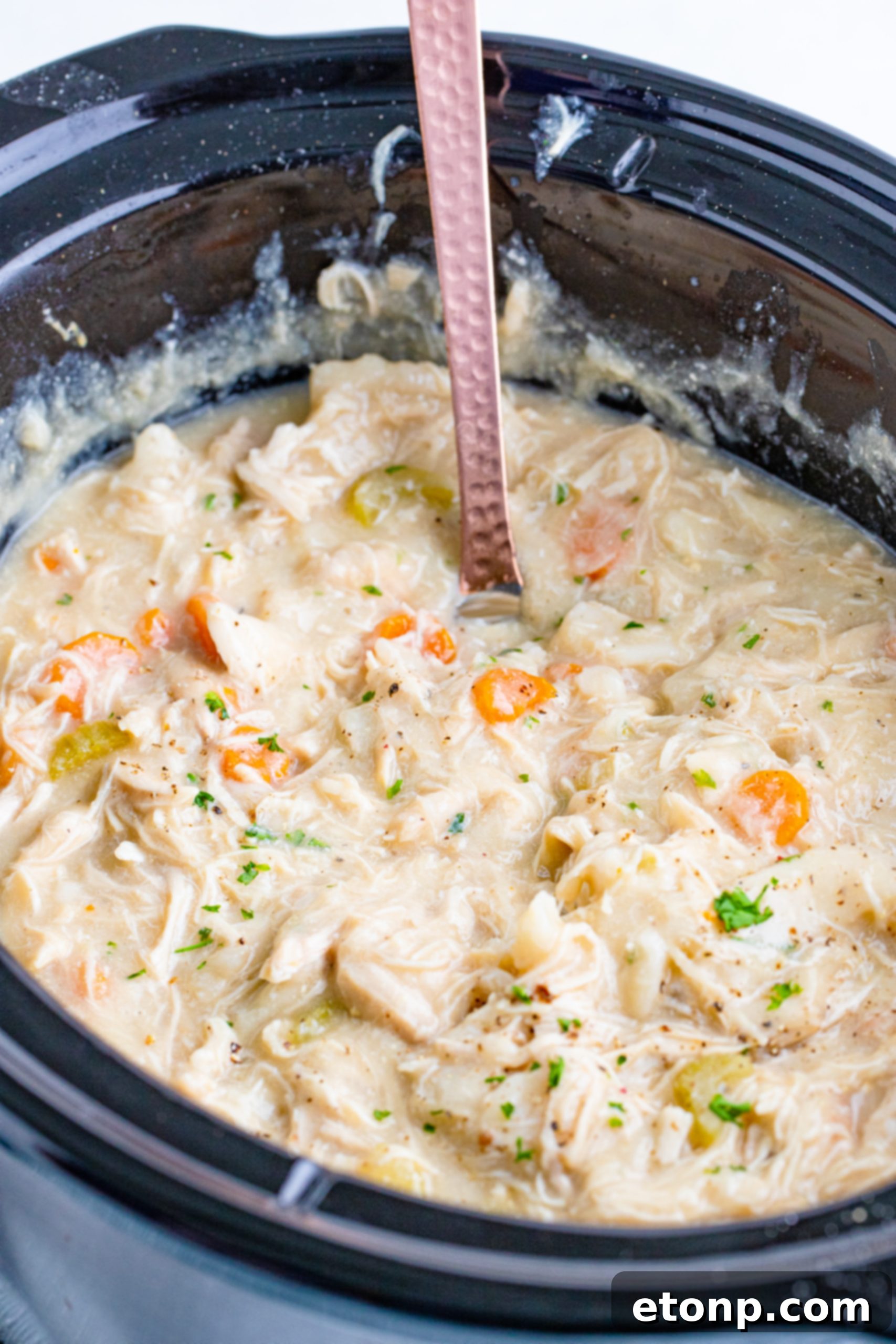 A person adding fresh vegetables into a slow cooker alongside other ingredients, symbolizing easy meal preparation.
