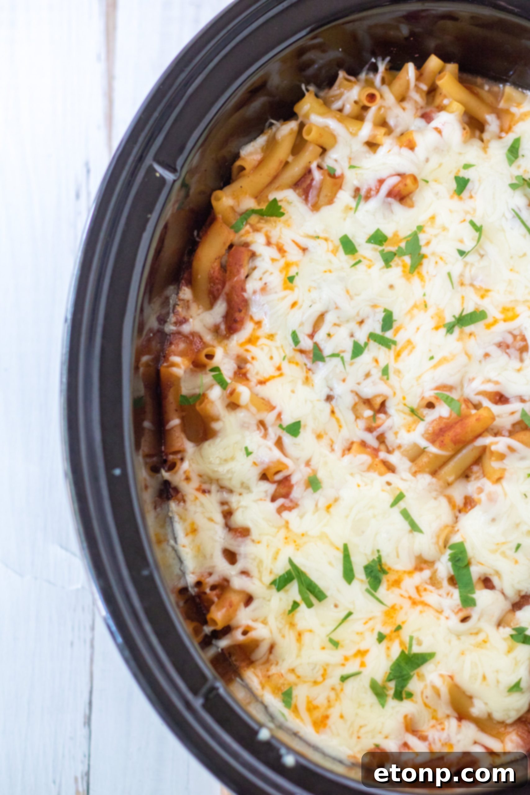 Scoop of Slow Cooker Cheesy Baked Pasta being lifted from the crock pot, showing cheesy goodness.