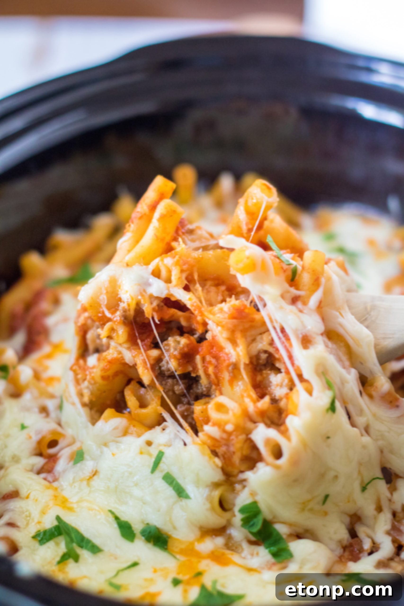 A generous serving of Slow Cooker Cheesy Baked Pasta in a white bowl, garnished with fresh herbs.