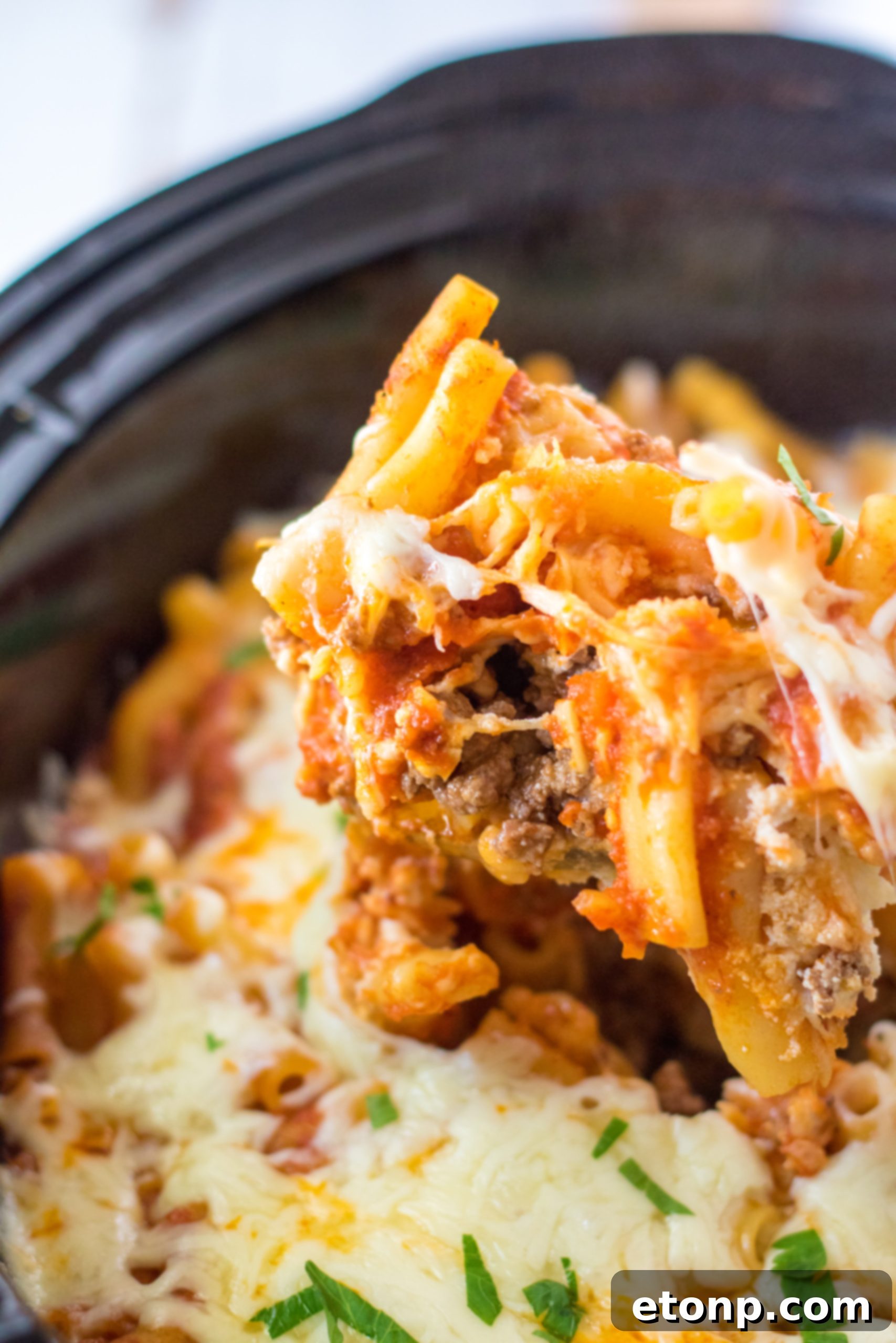 Hands preparing the Slow Cooker Cheesy Baked Pasta, layering ingredients into the crock pot.