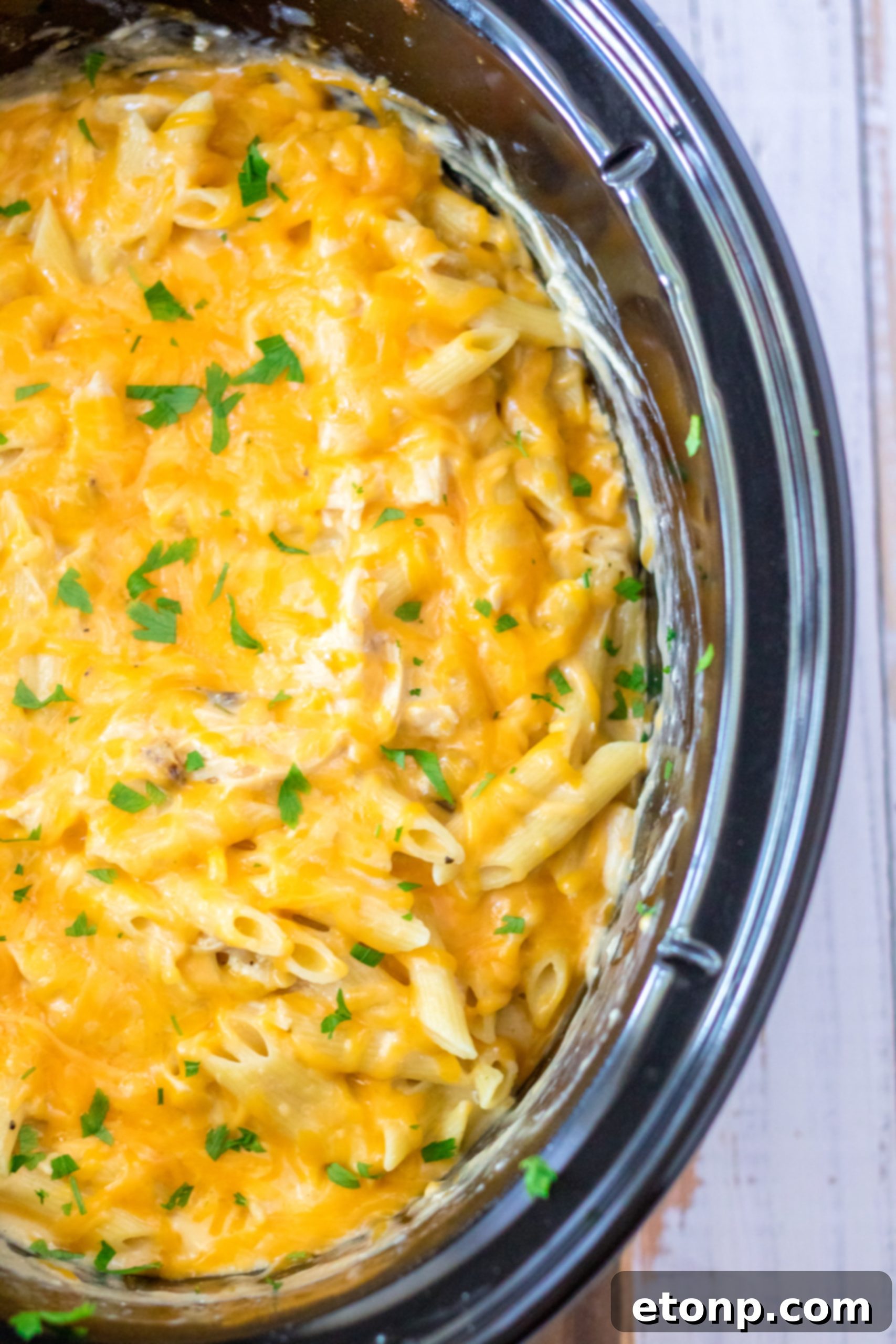 A large serving spoon scooping the Cheesy Chicken Penne from the slow cooker