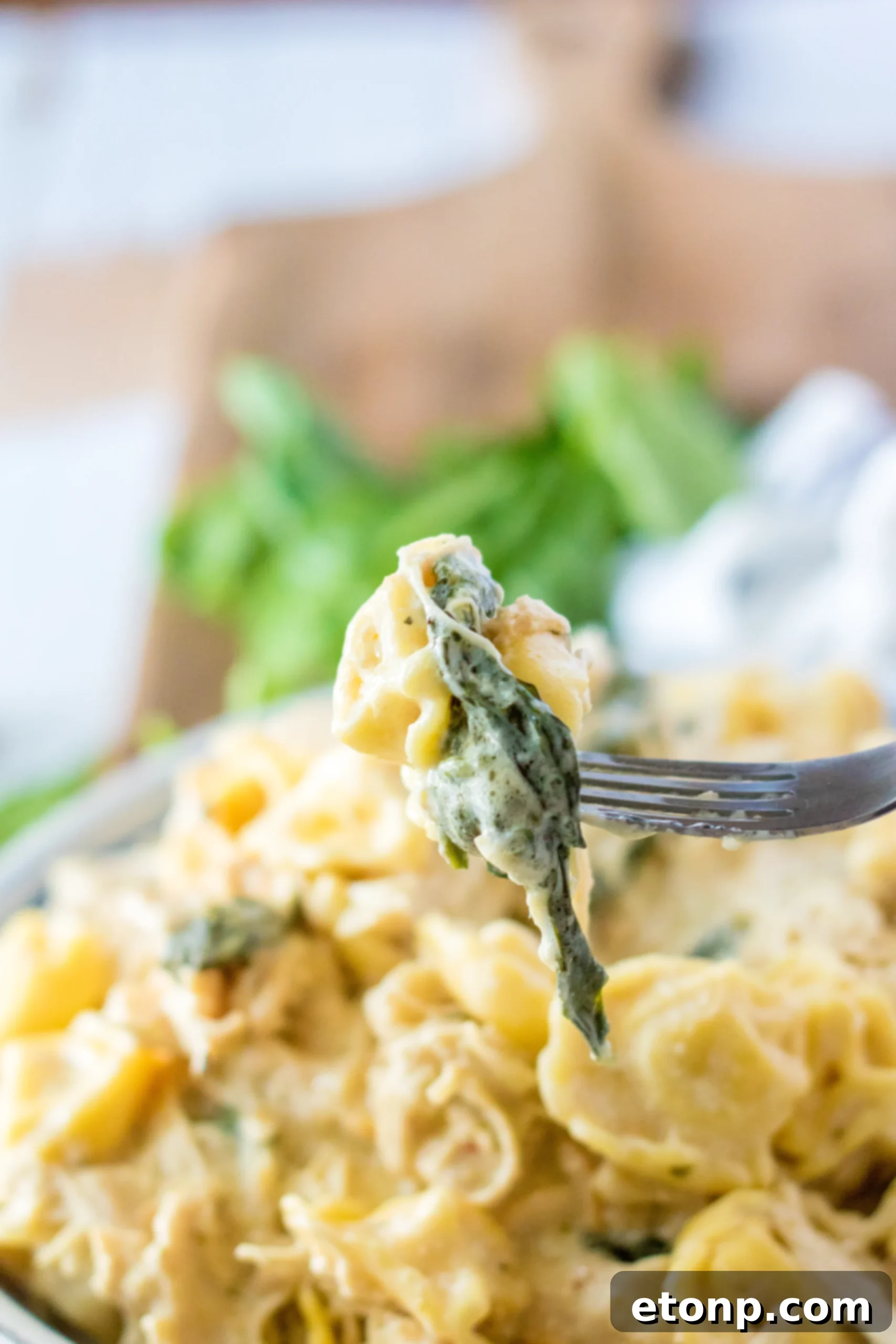 A spoon scooping a generous portion of slow cooker creamy chicken tortellini from a pot.