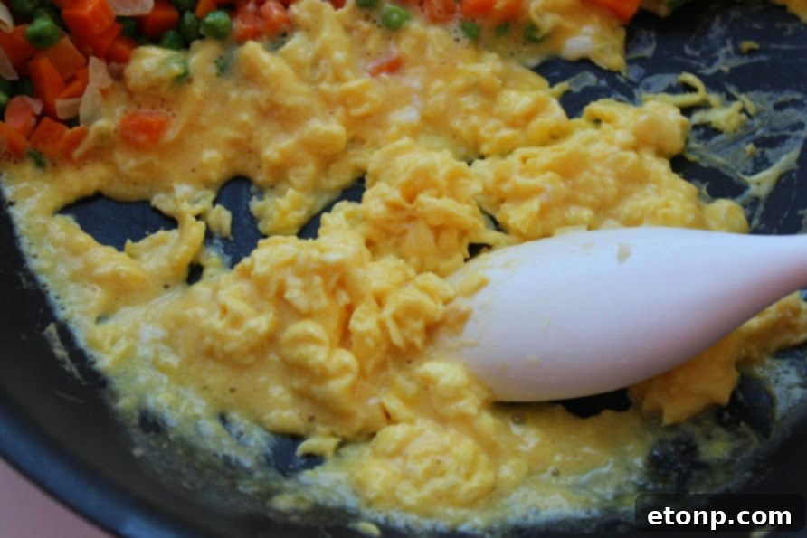 A hand stirring fried rice in a pan, showcasing the golden color and texture.