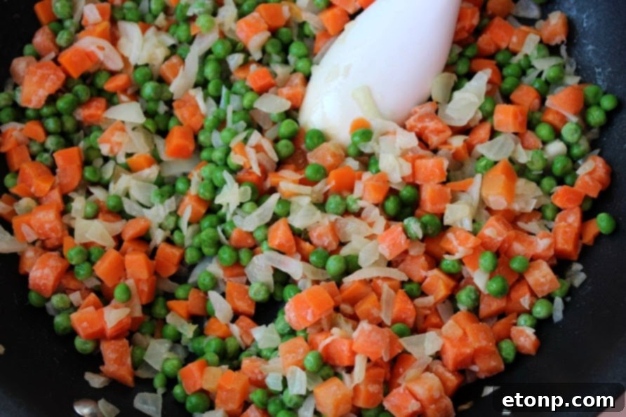 Frozen peas and carrots being added to a hot pan with other ingredients.