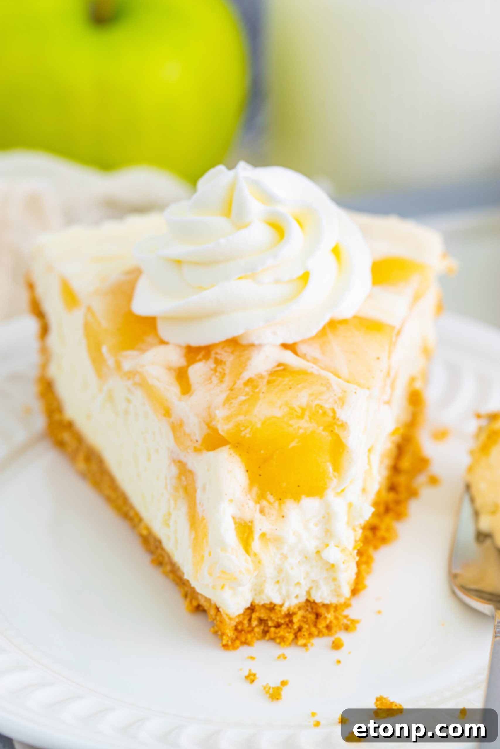 A beautifully sliced No Bake Apple Cheesecake, showcasing its creamy filling and chunky apple topping on a rustic wooden board.
