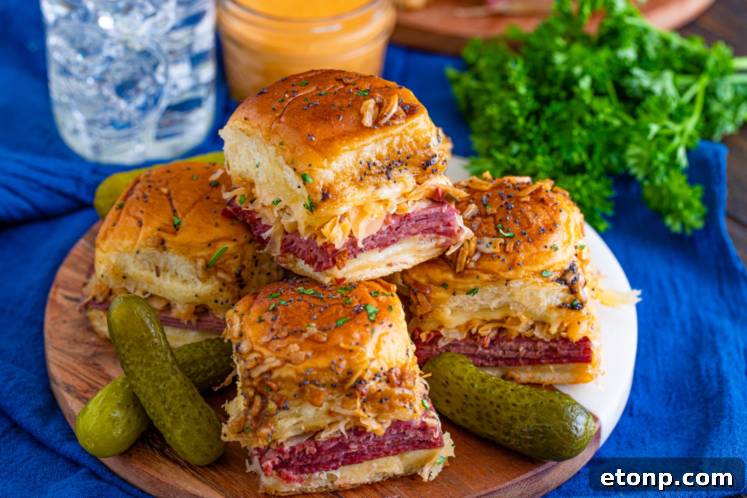 Mini Reuben Sandwiches 13 Two hands reaching for freshly baked Reuben Sliders from a baking dish, highlighting their appeal.
