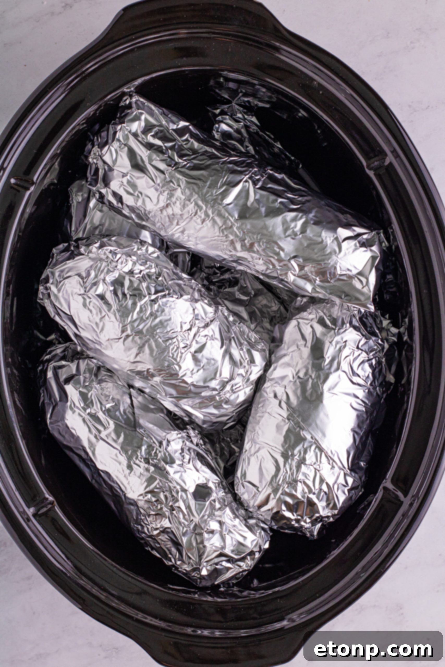 A slow cooker filled with foil-wrapped potatoes