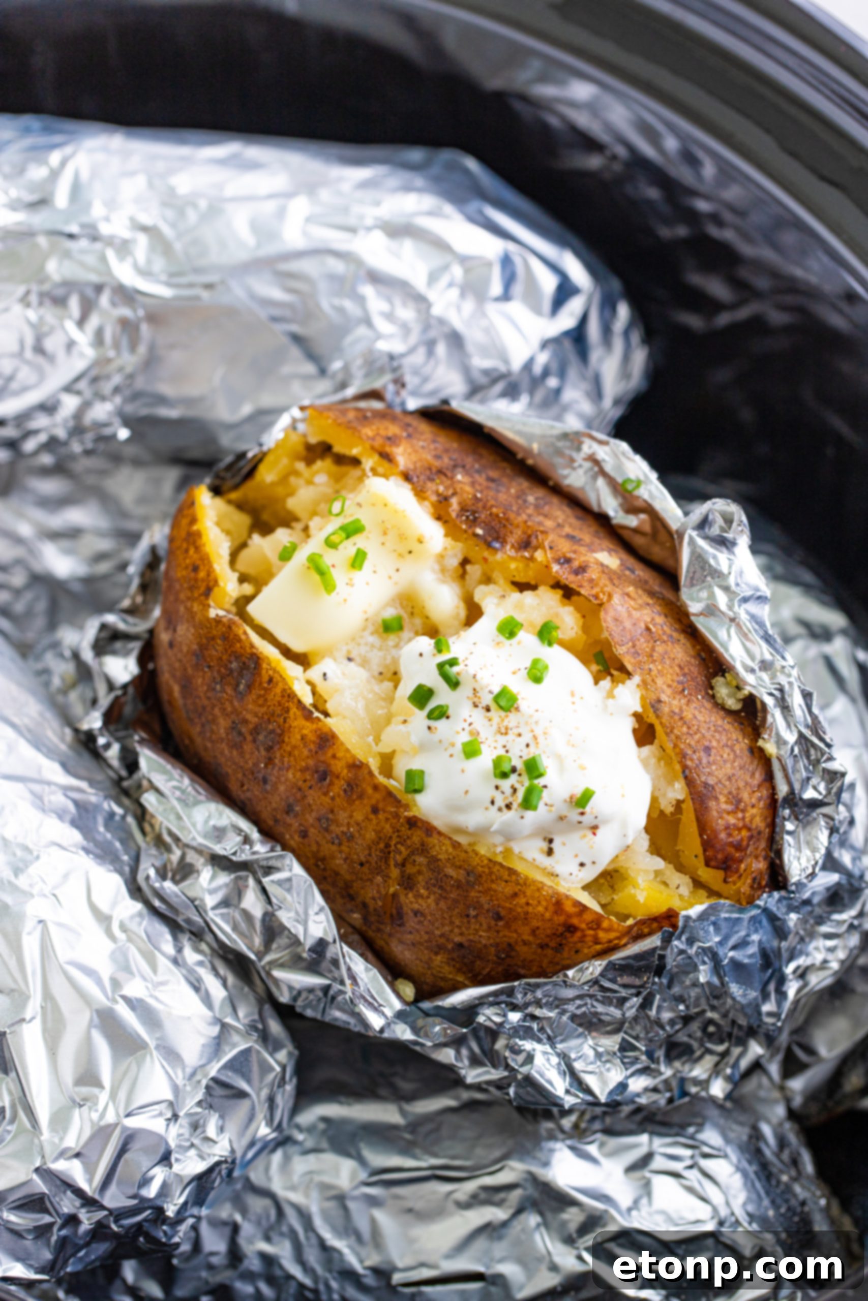 Topping a slow cooker baked potato with sour cream and chives