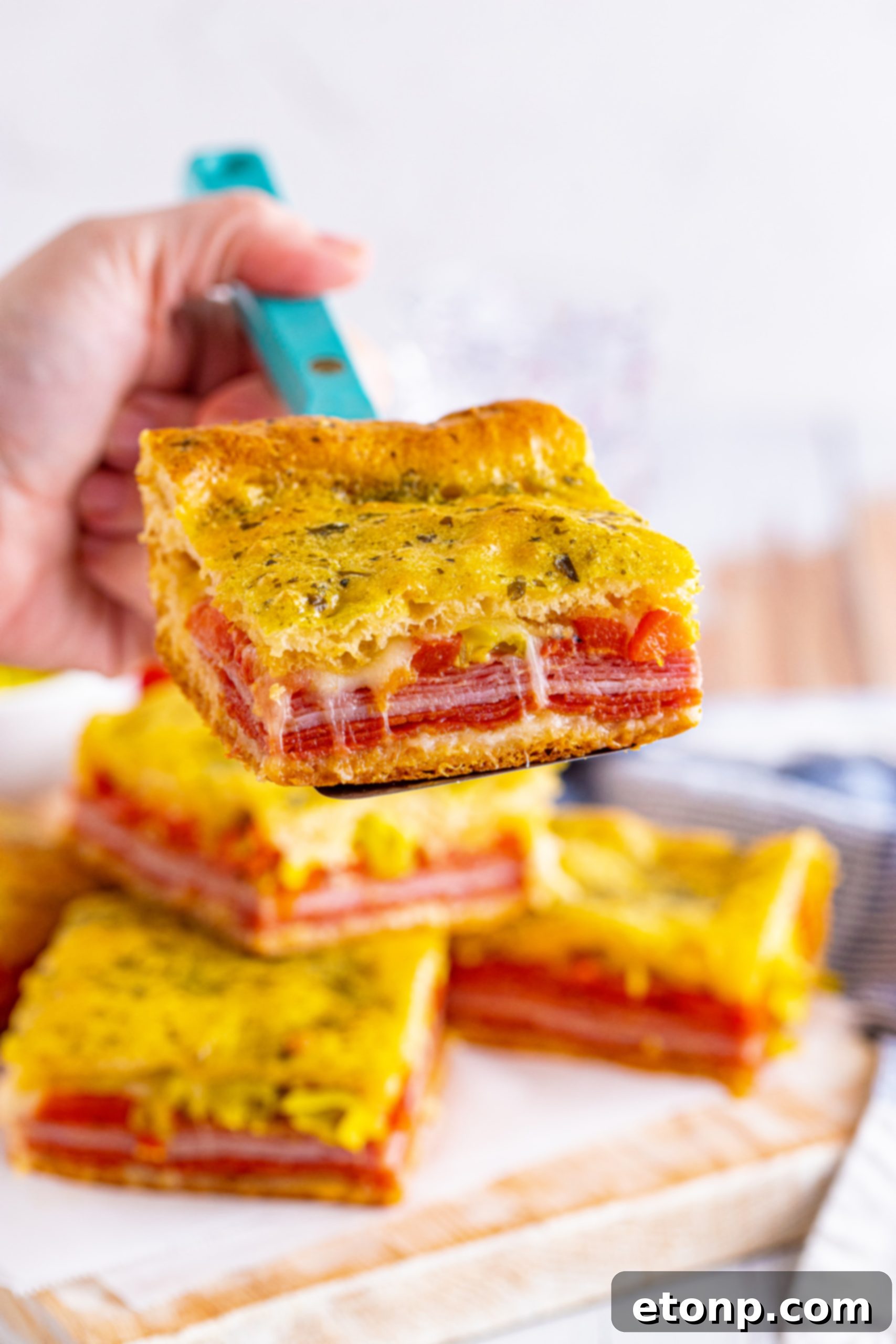 Two pieces of Italian Antipasto Squares on a parchment-lined baking sheet, prepared for reheating in the oven.