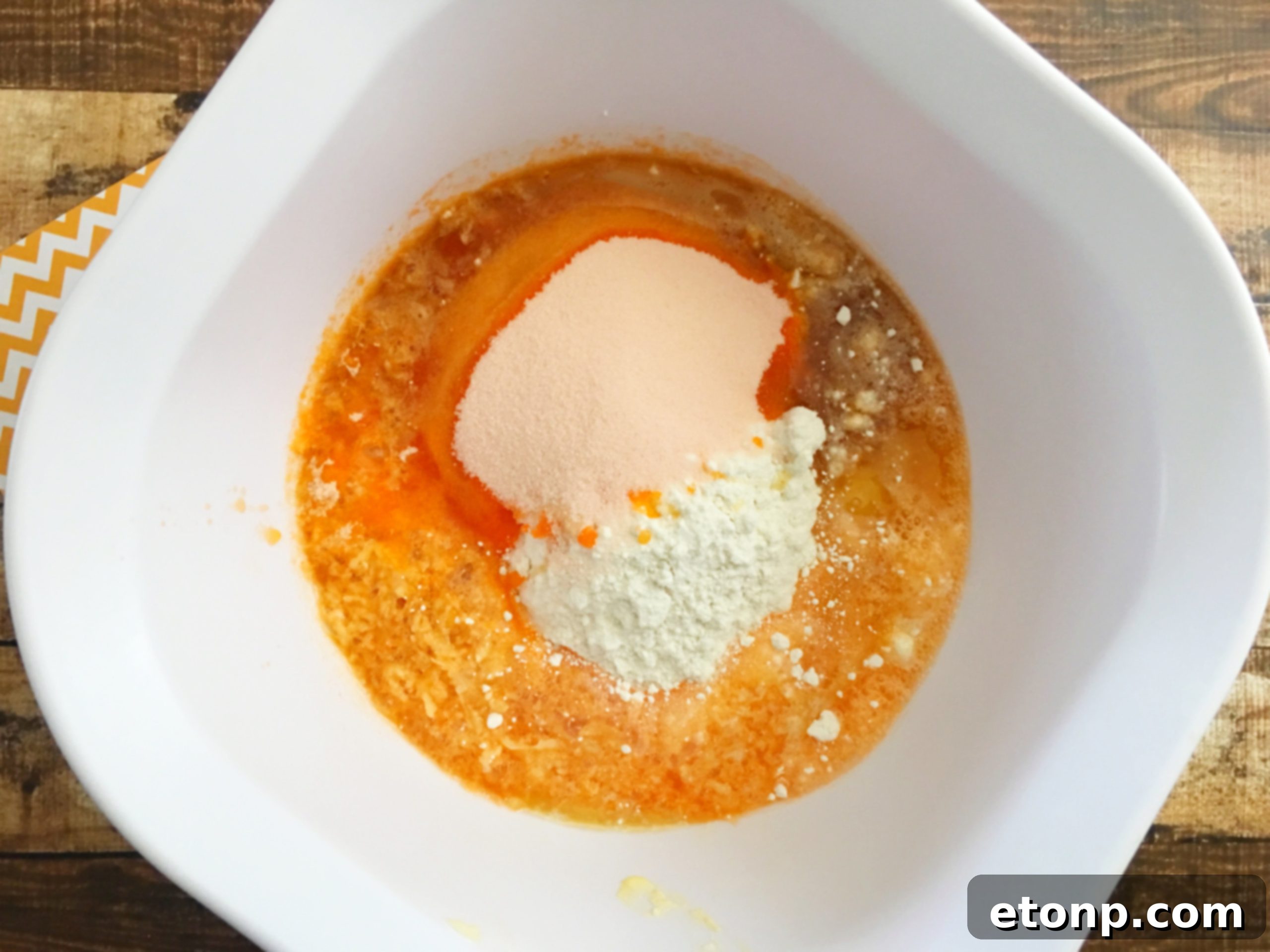 A hand holding a perfectly frosted Orange Creamsicle cupcake, garnished with a colorful paper straw