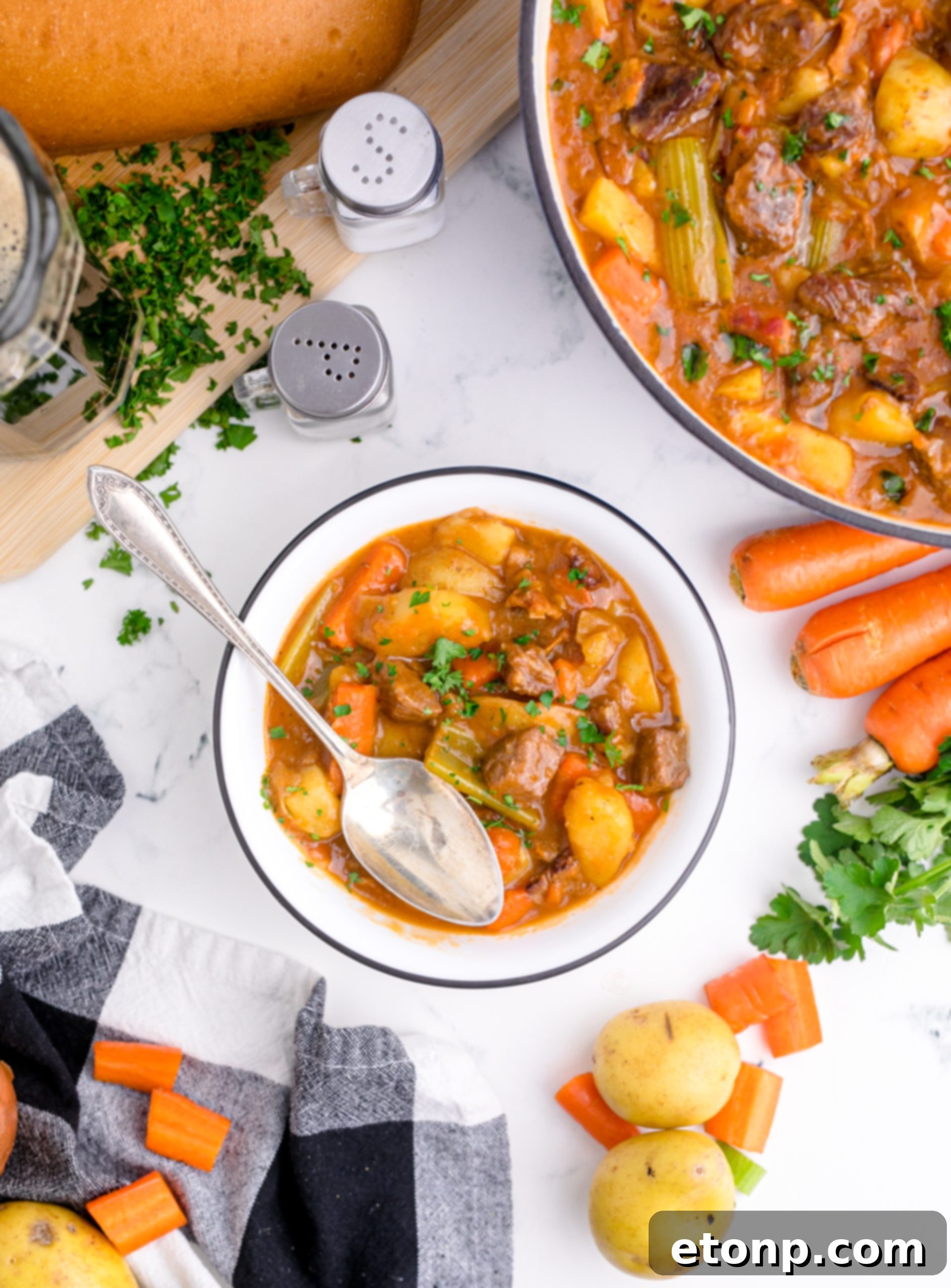 Various ingredients for Guinness Beef Stew laid out on a wooden cutting board, including seasoned beef, chopped vegetables, and a bottle of Guinness.