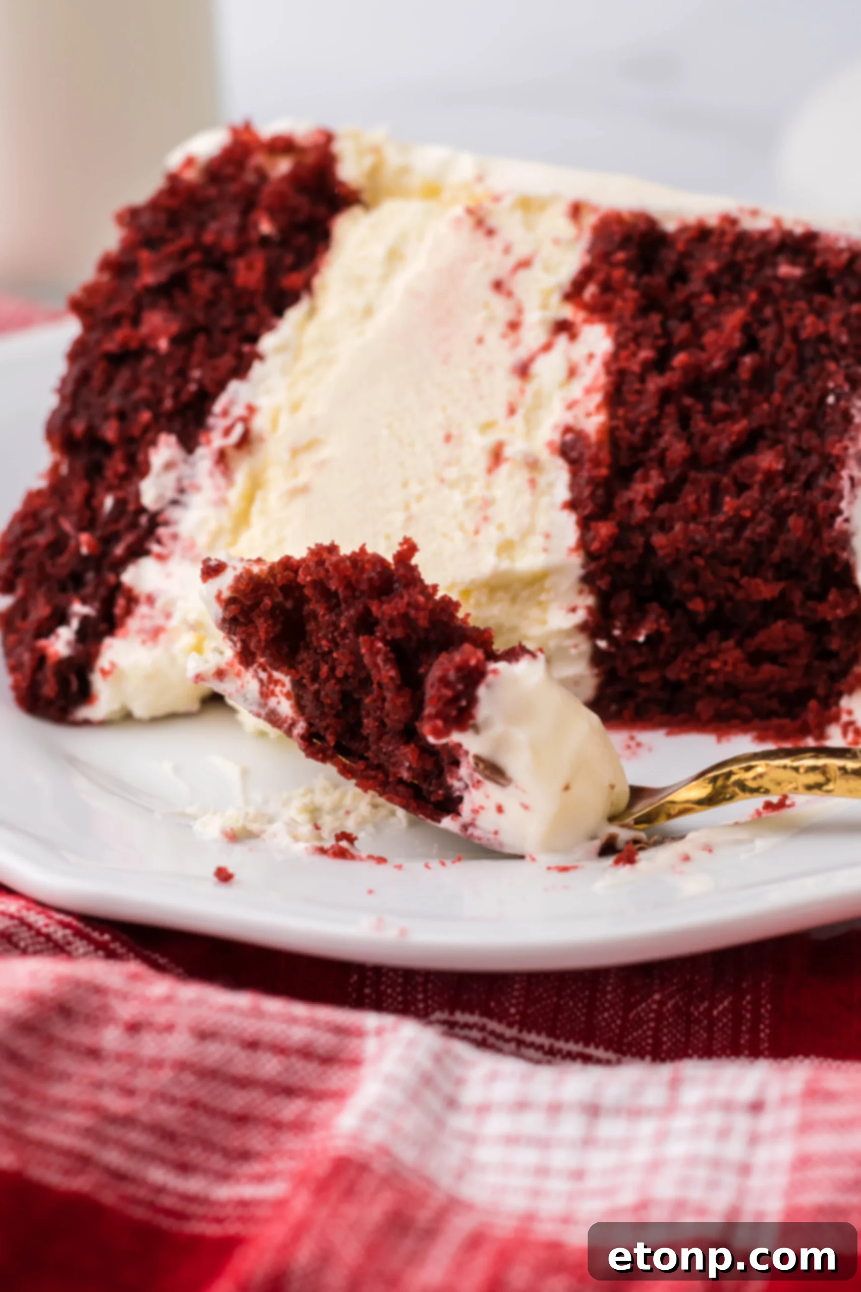 A slice of Red Velvet Cheesecake Cake, showing the distinct red velvet cake layers and the creamy cheesecake in the middle, topped with white cream cheese frosting.